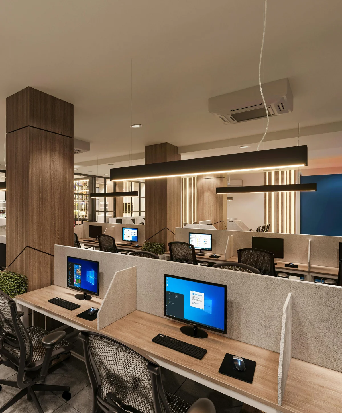 A modern open-plan office features multiple computer workstations with light wood desks, grey dividers, and black mesh chairs.