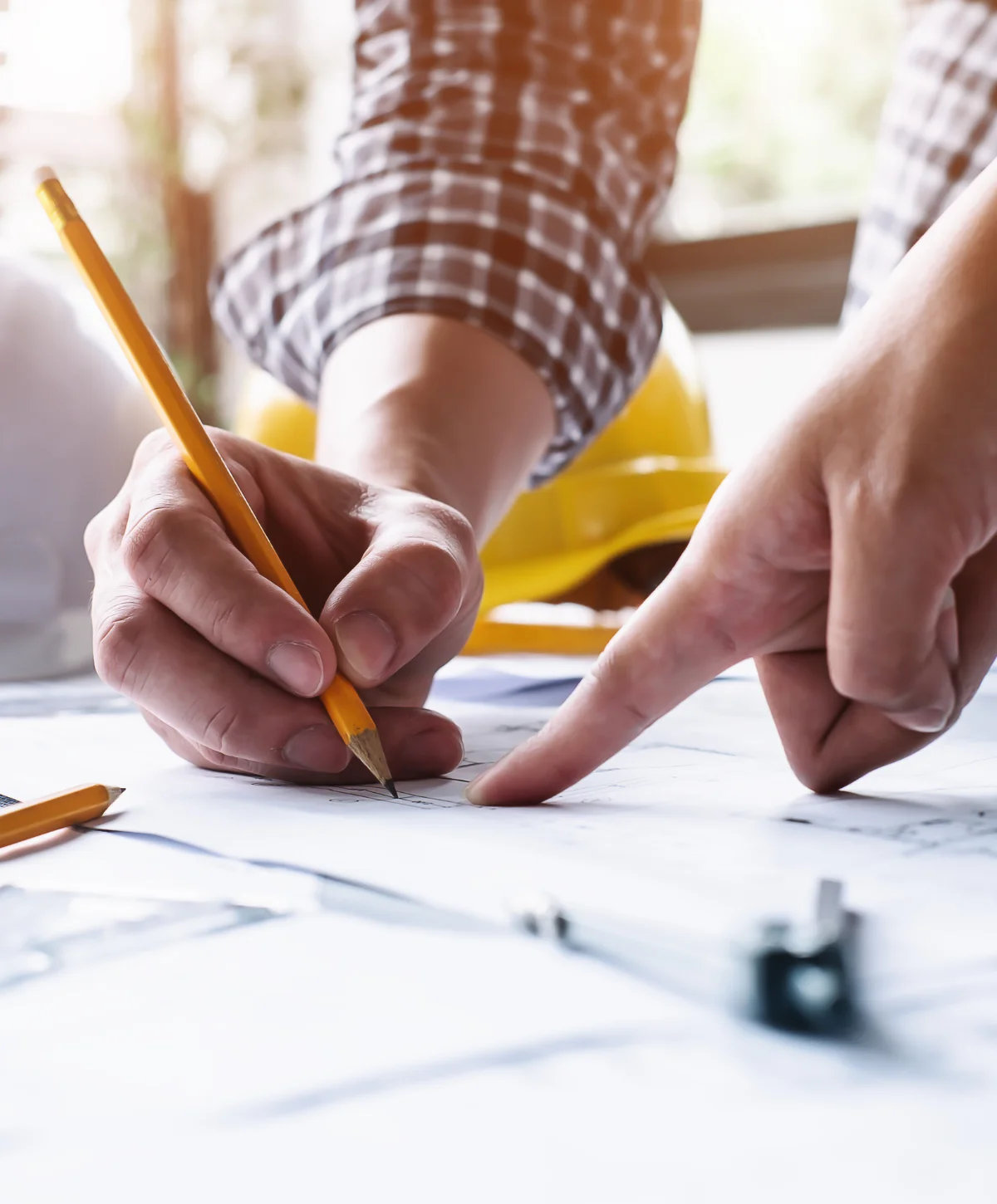 Close-up of two people's hands working on architectural blueprints with a pencil and pointing at details.