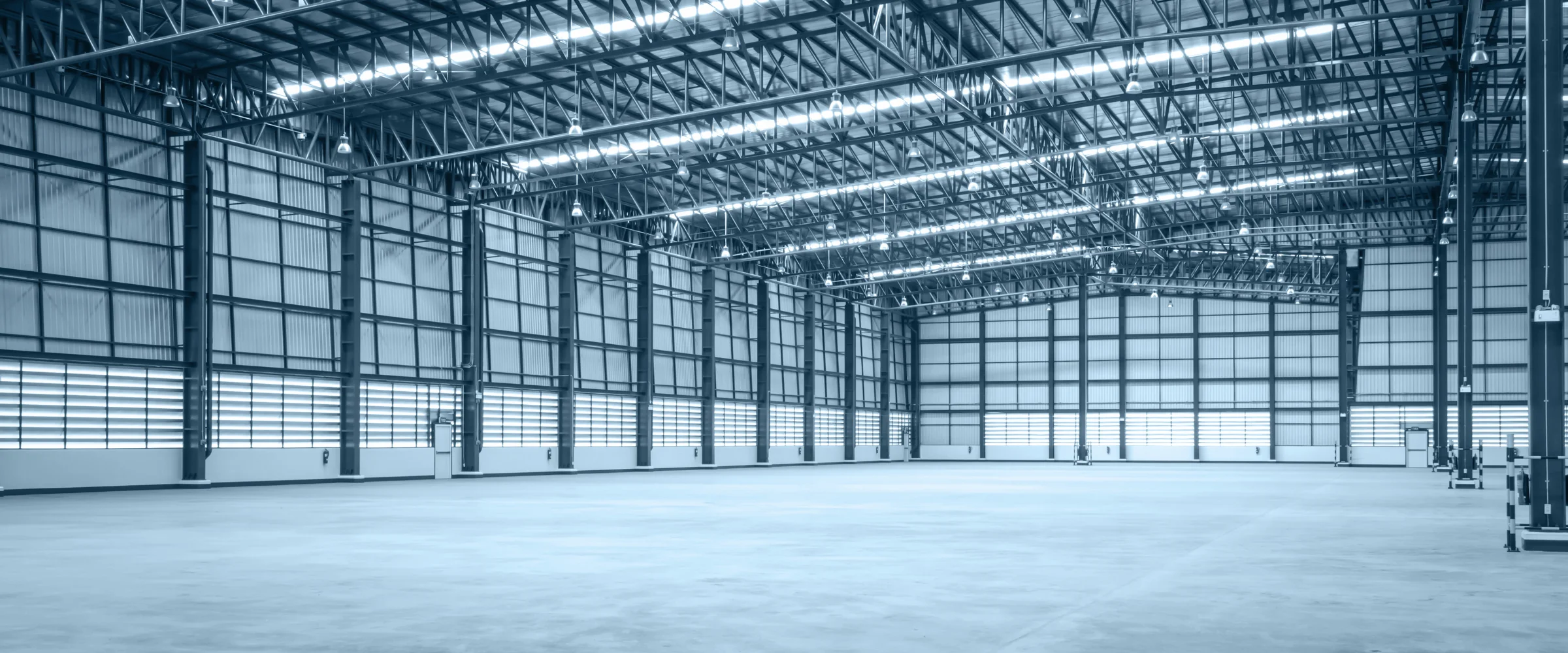 A wide view of a large, empty industrial warehouse interior with a high ceiling, metal trusses, and concrete floor.