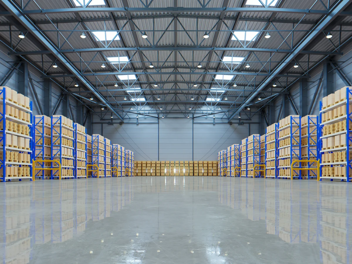 A long, empty aisle in a modern warehouse with rows of shelves stacked with cardboard boxes on pallets.