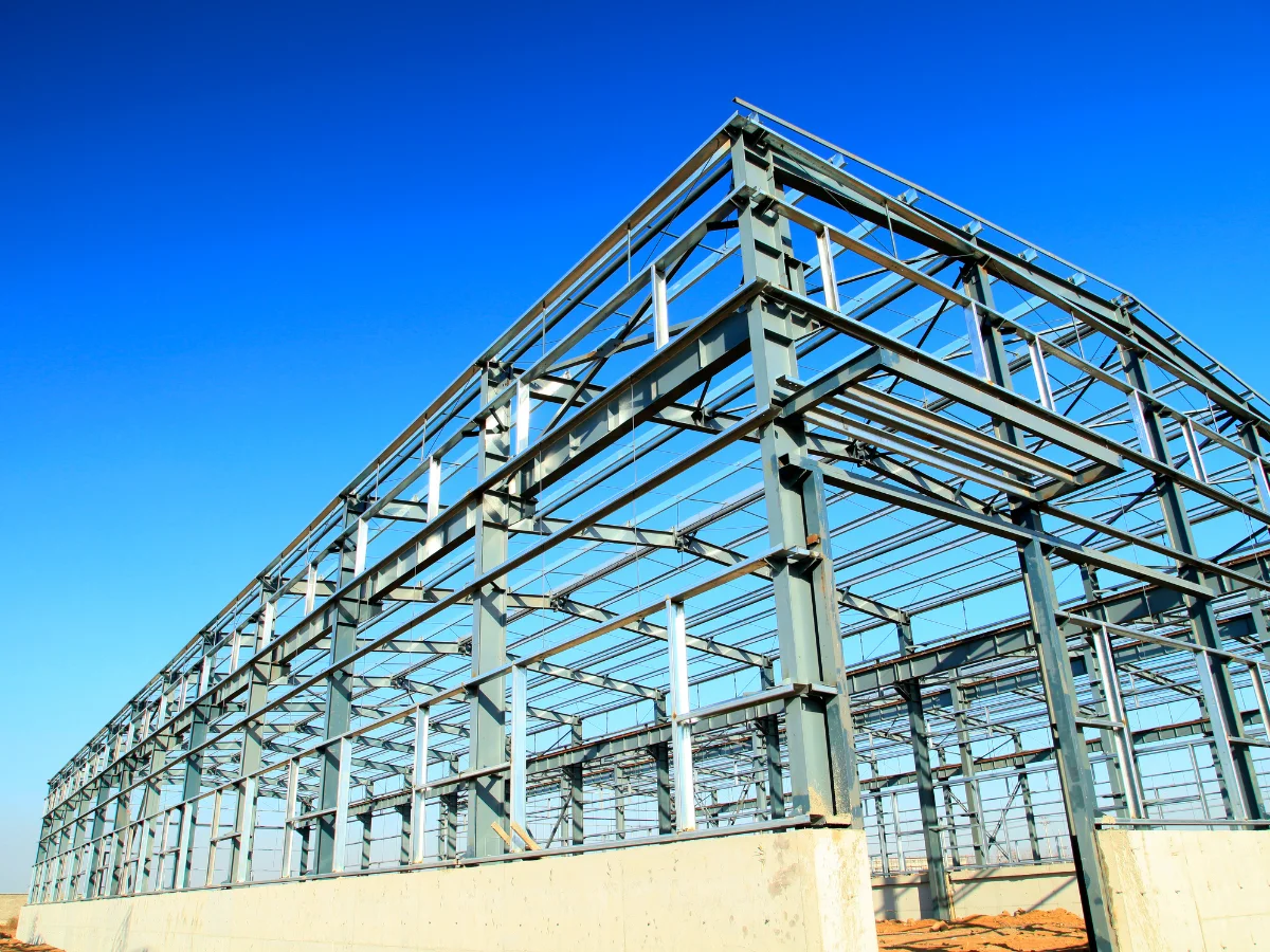 A large steel frame building structure under construction, viewed from a low angle against a clear blue sky.