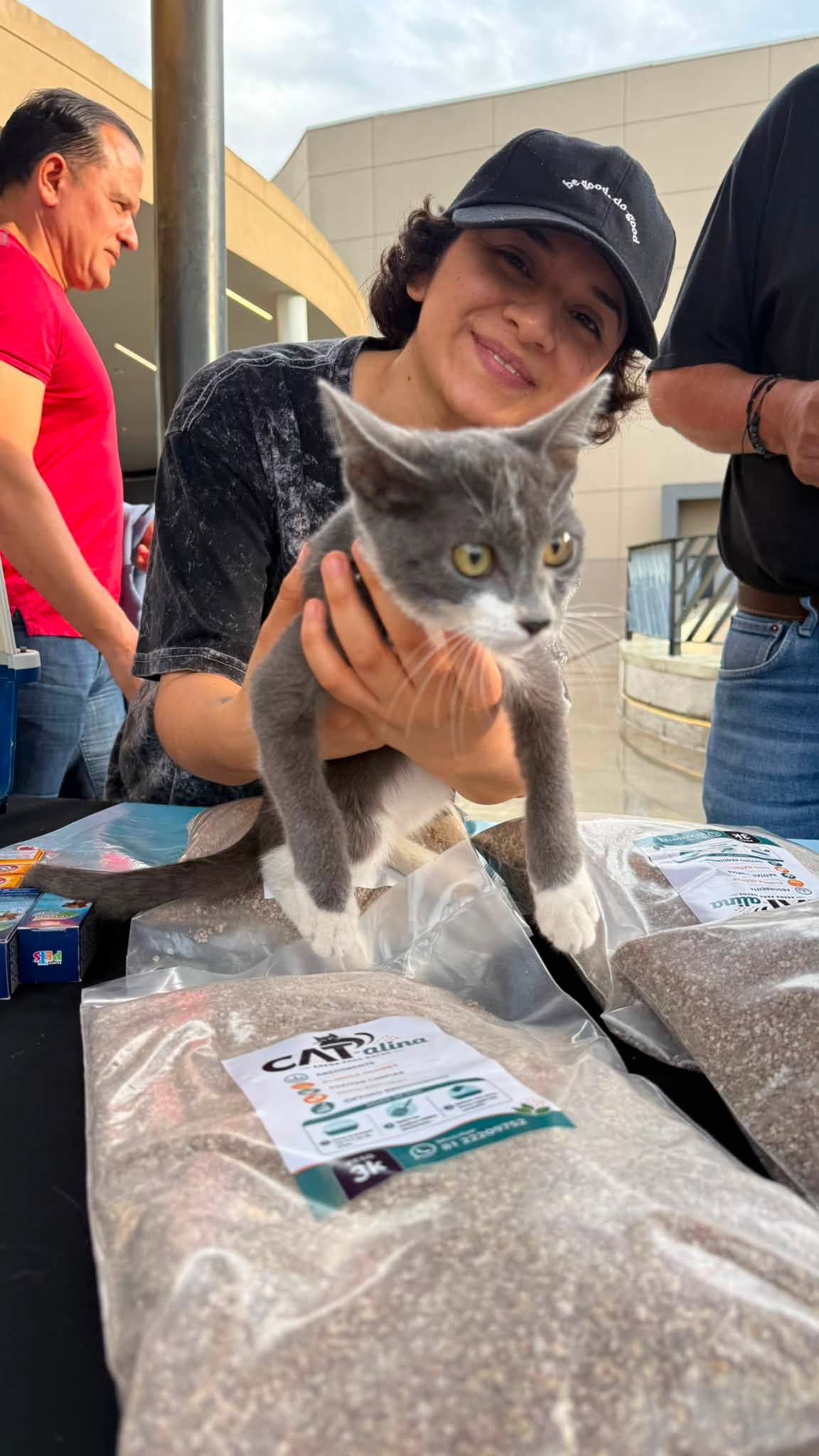 Voluntaria con un gato gris junto a bolsas de CAT-alina
