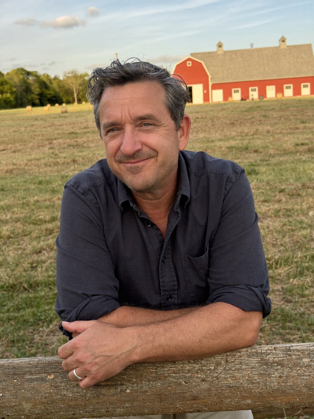 Eric Lay leaning on a fence rail in front of a red barn