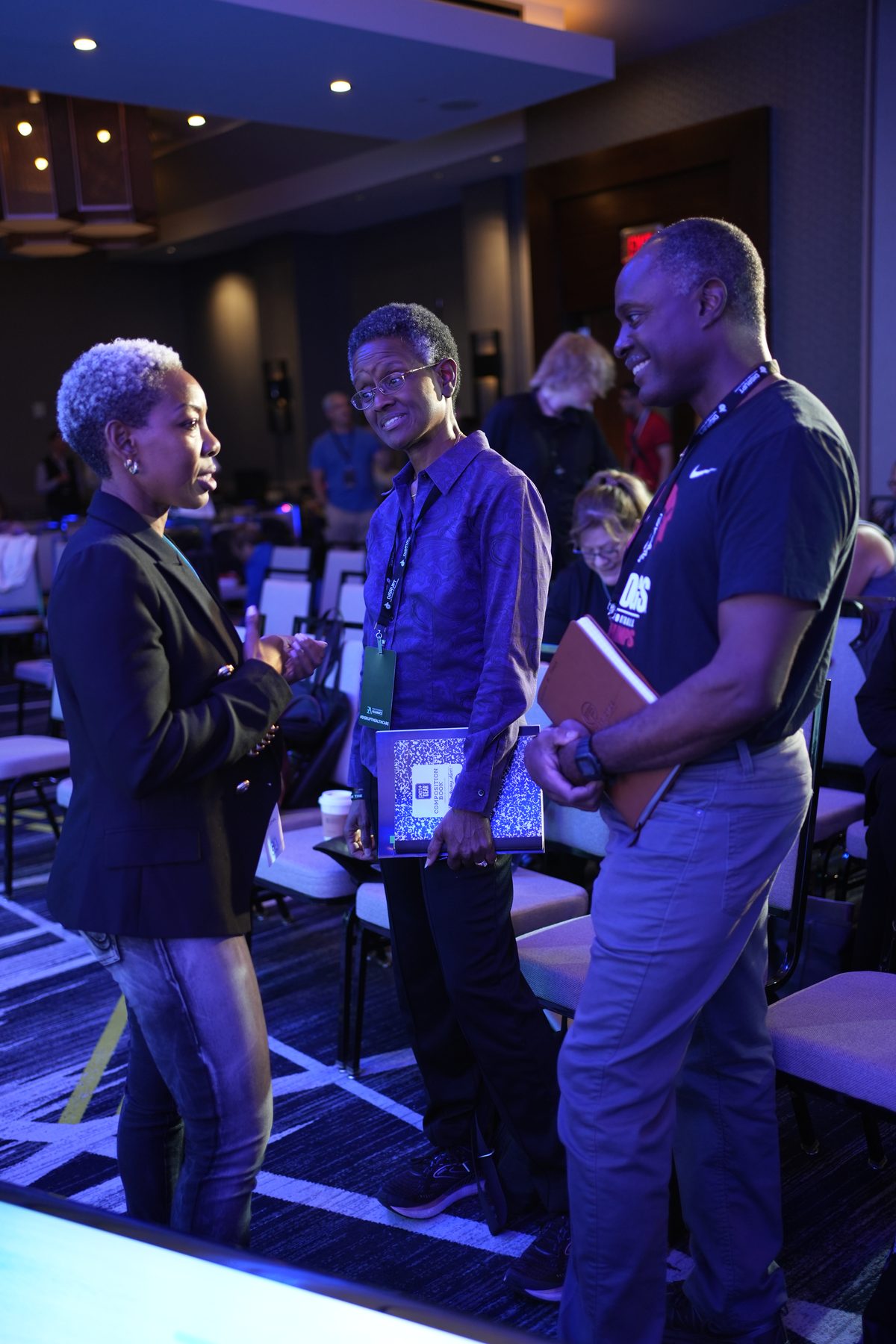Three members with notebooks talking and smiling in the ballroom aisle