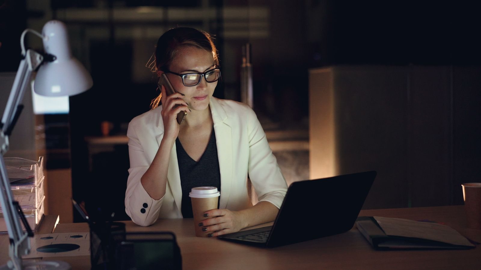 A practitioner working late at night, on the phone with a laptop and coffee