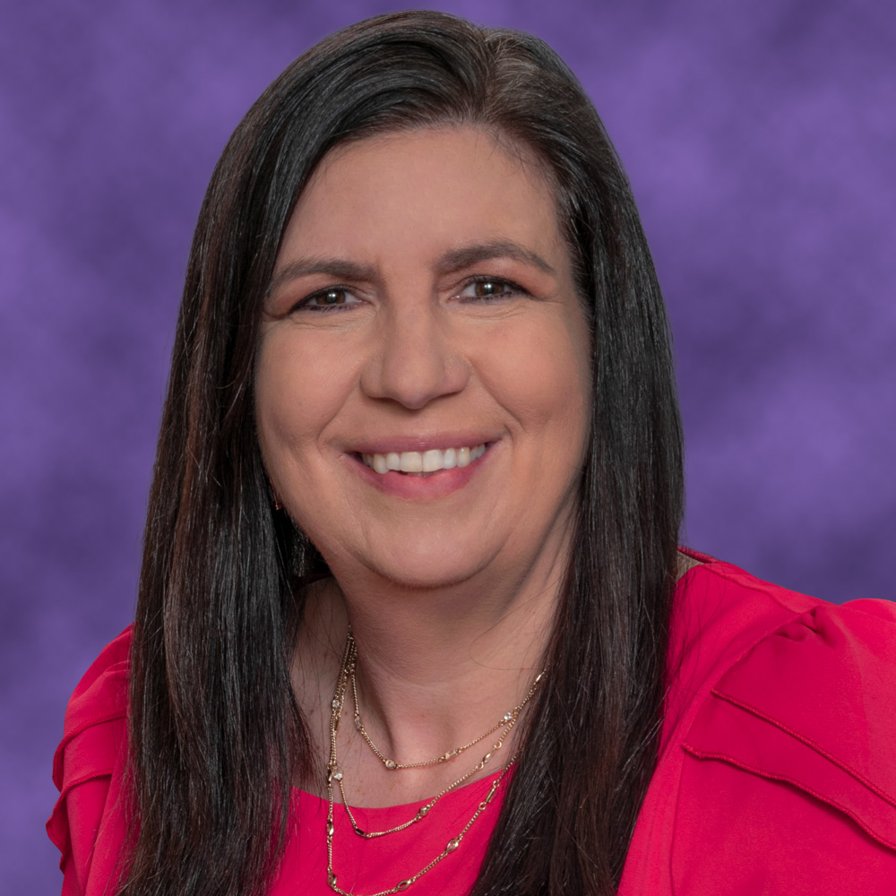 Michele Kostedt smiling, in a rose-colored top against a purple background