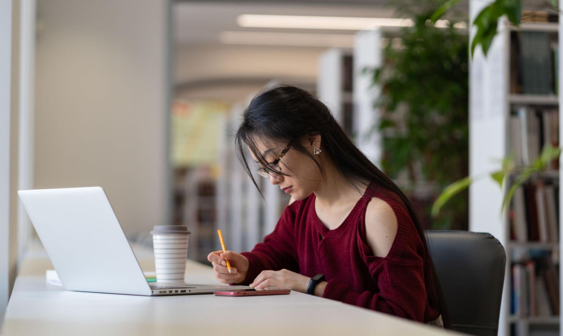 A student actively researching on a laptop, with a notebook or planner nearby.