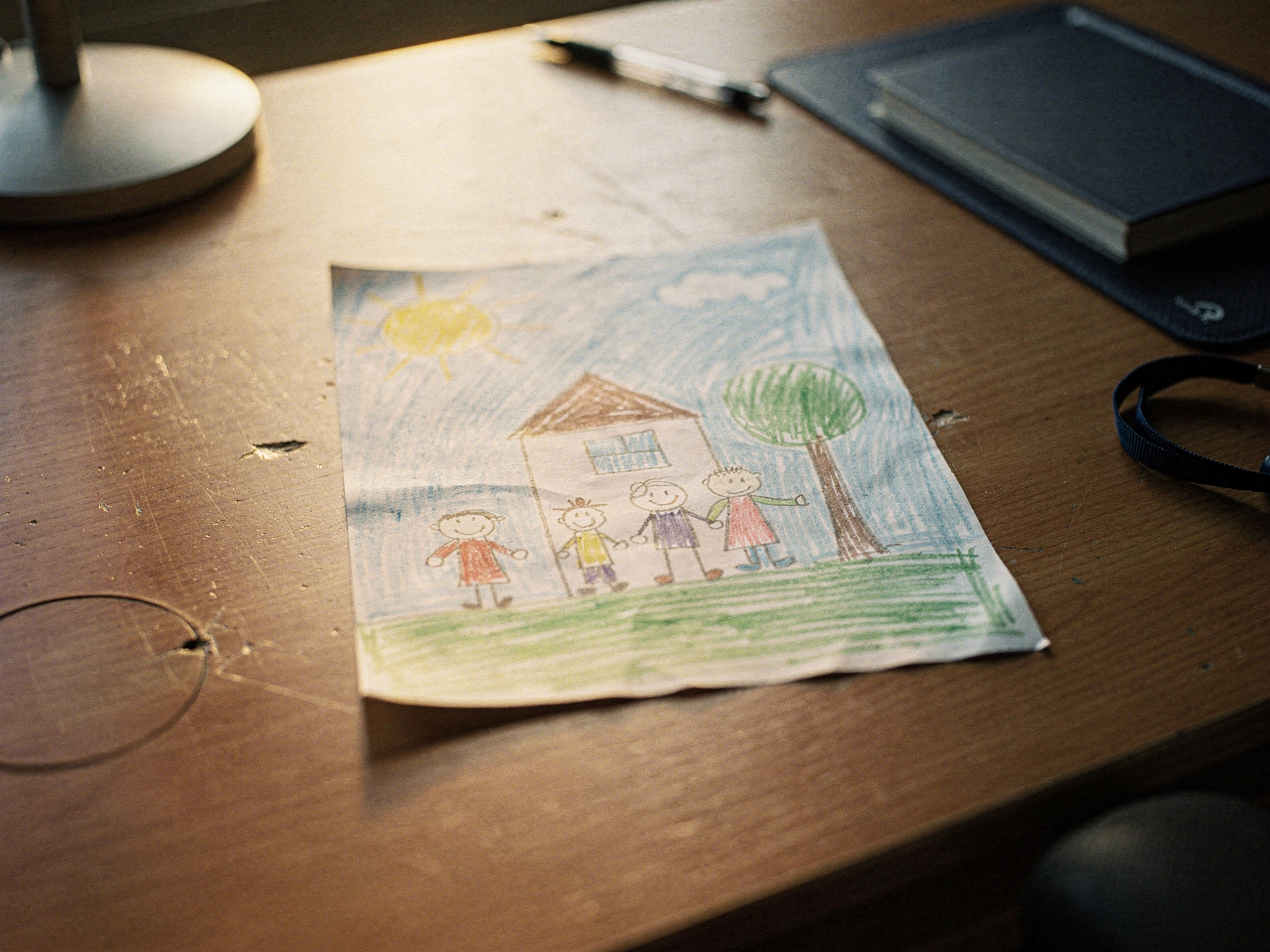 A child's crayon drawing of a family and a house resting on a desk.