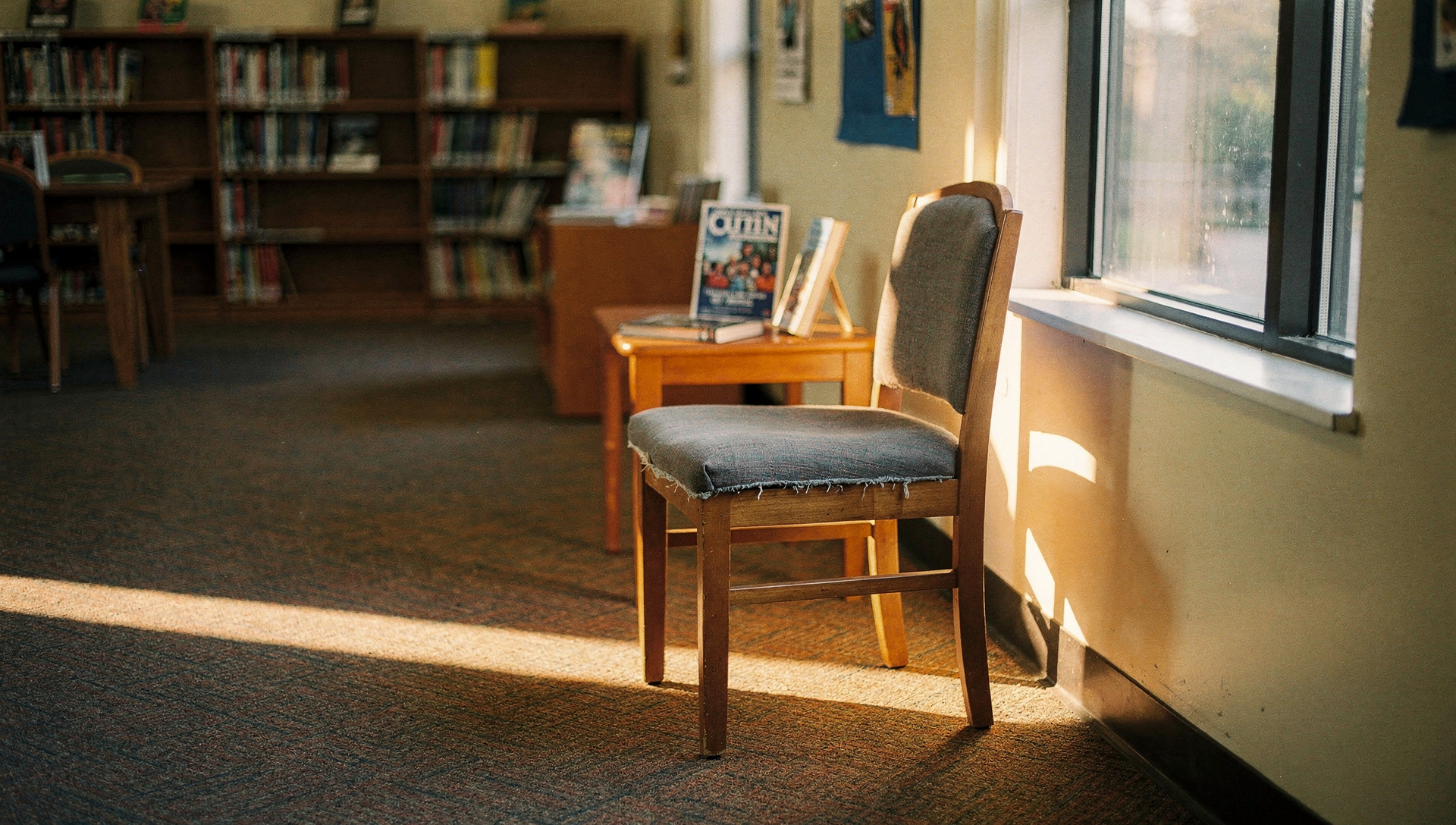 A quiet school library reading nook with a single empty chair in warm afternoon light.