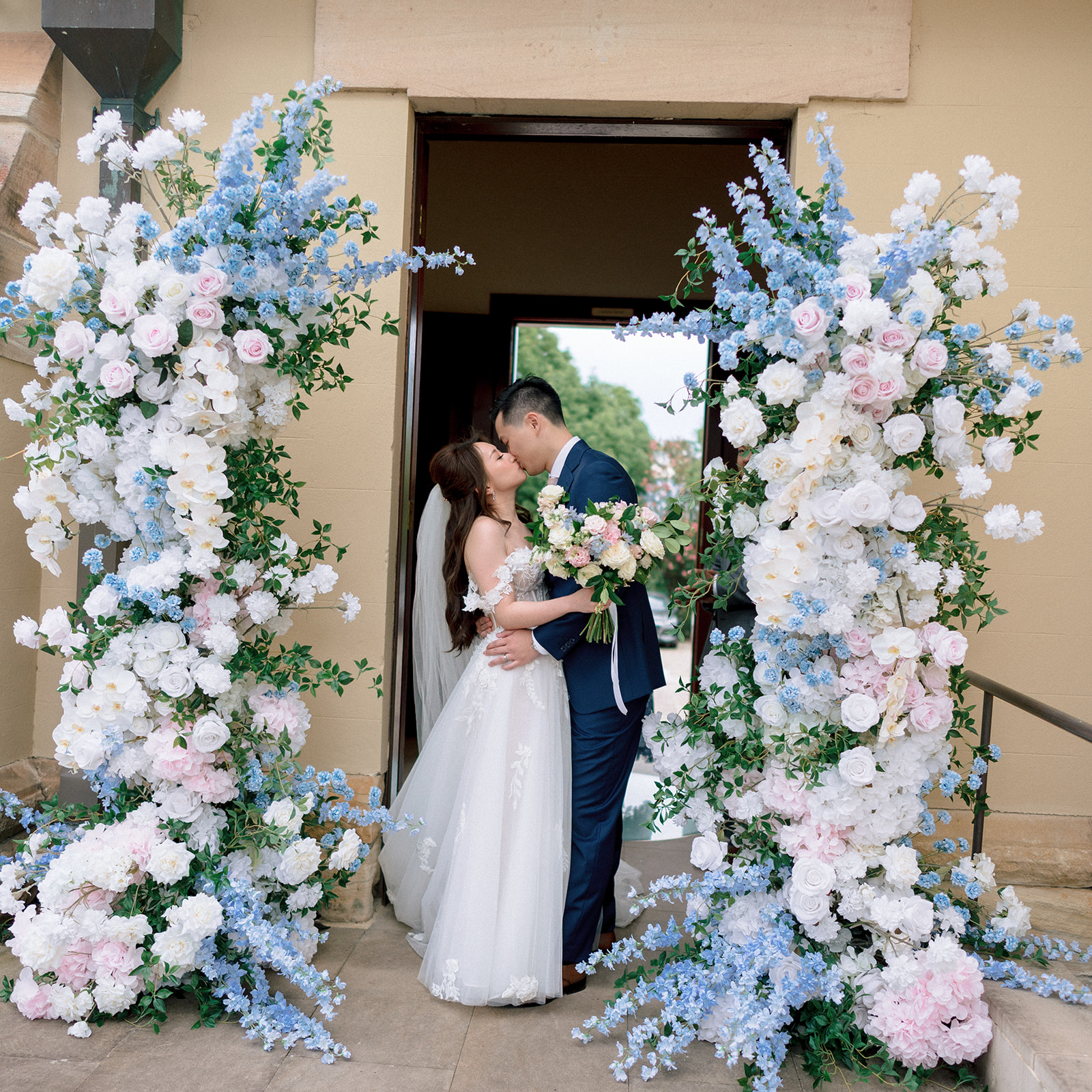 Couple kissing between blue and blush floral pillars