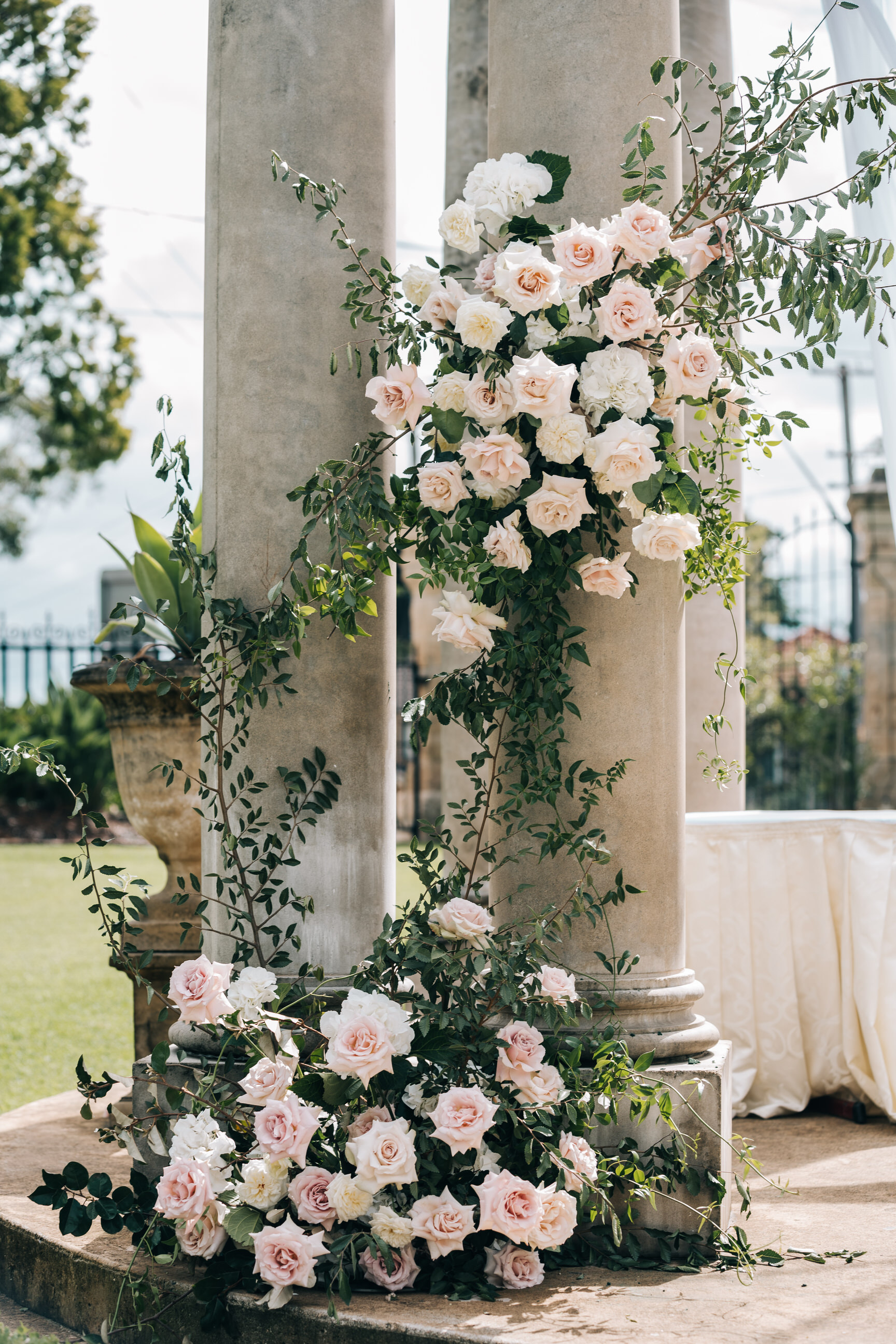 Blush roses climbing a stone column at an outdoor ceremony
