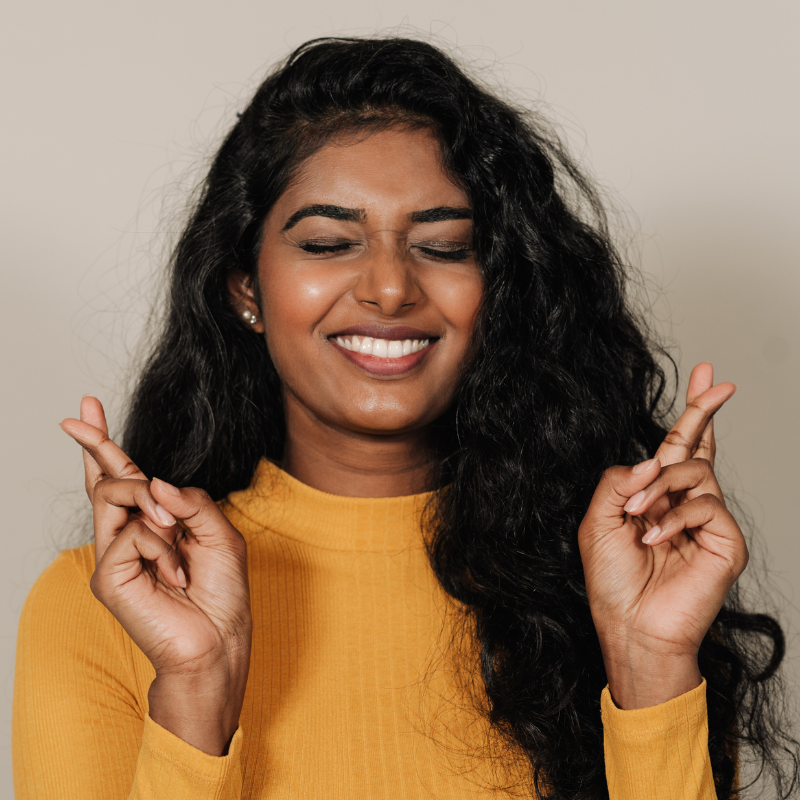 smiling woman with her eyes closed and fingers crossed