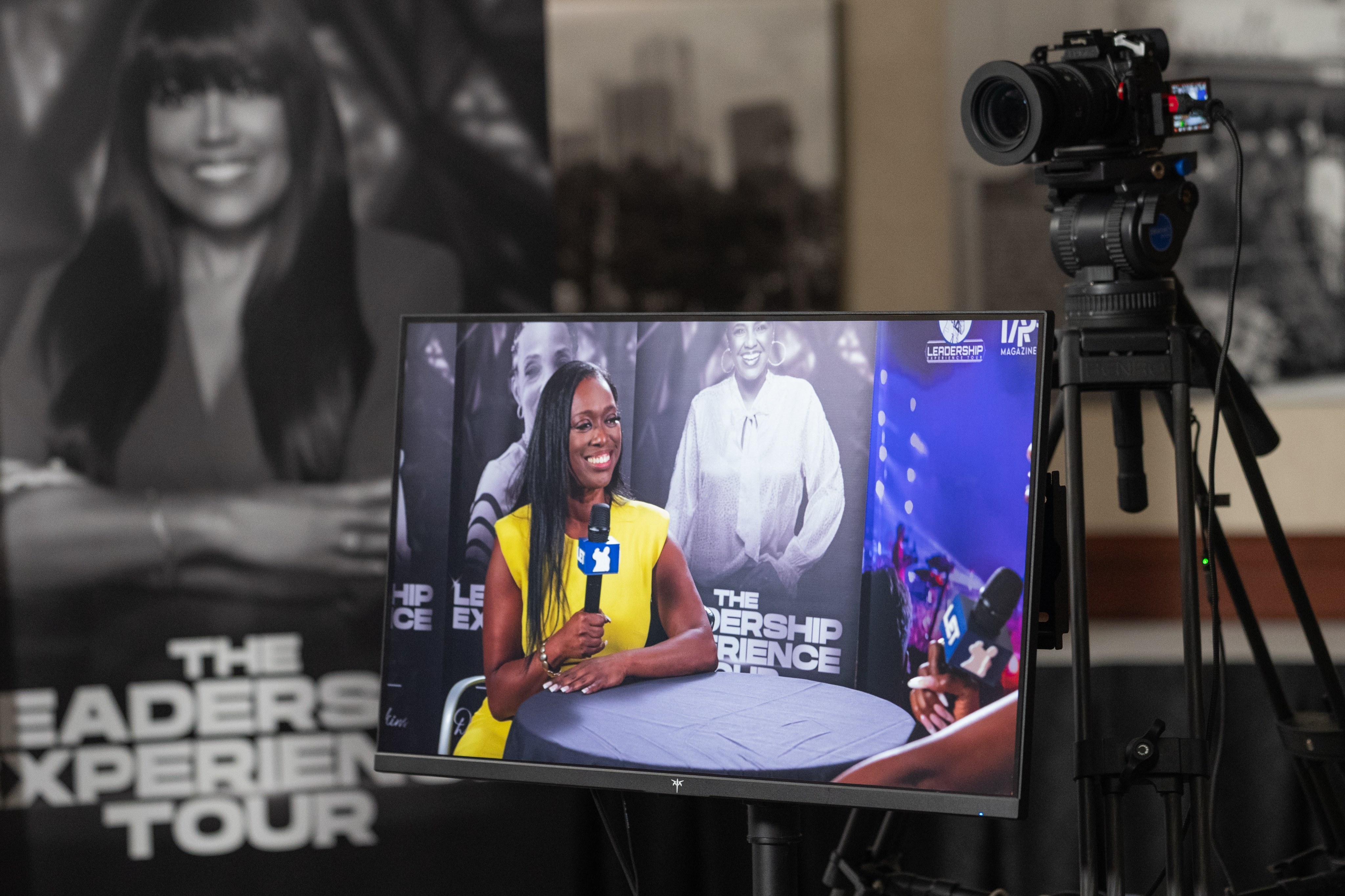 A camera and monitor framing a guest interview on a branded Leadership Experience Tour set