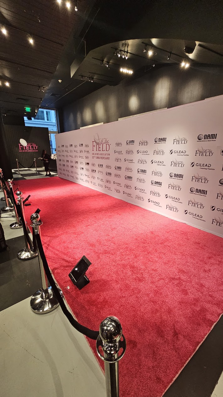 An empty pink carpet roped off with silver stanchions in front of the Off The Field sponsor wall before the doors opened