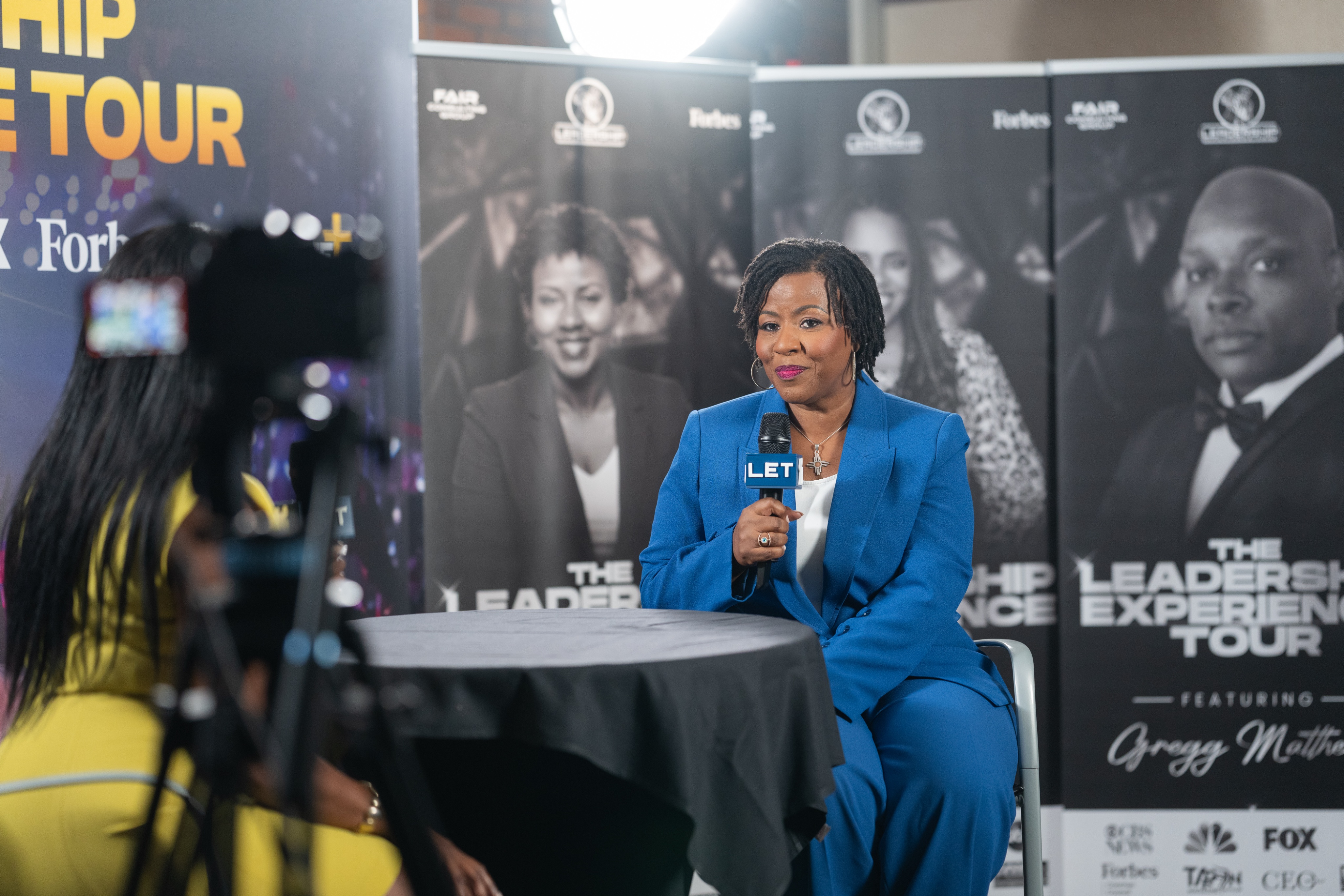 A guest in a blue suit interviewed on a Leadership Experience Tour set with a branded mic flag