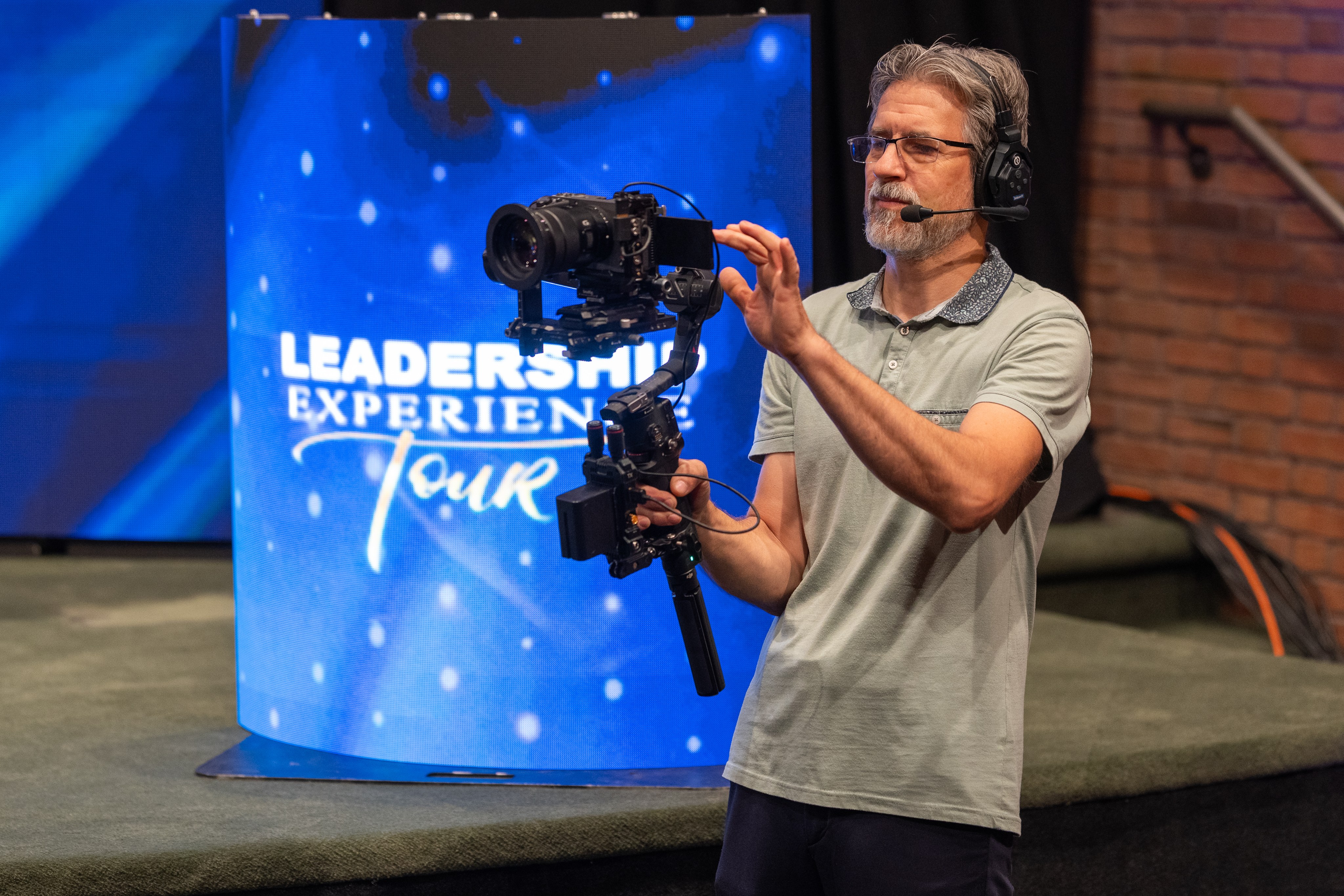 A camera operator flying a gimbal camera in front of a lit event backdrop