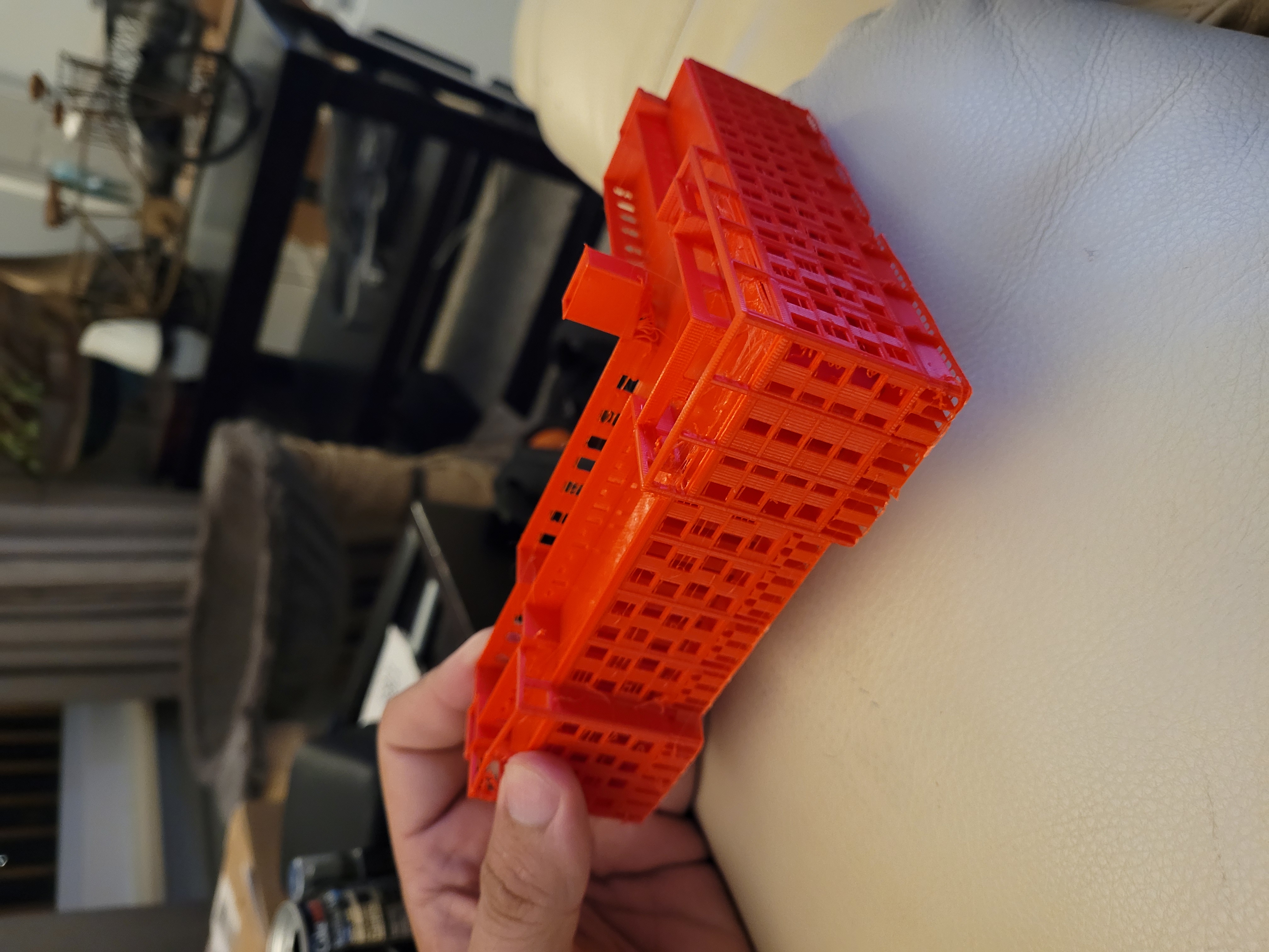 A large format 3D printer building a red architectural part on its heated bed
