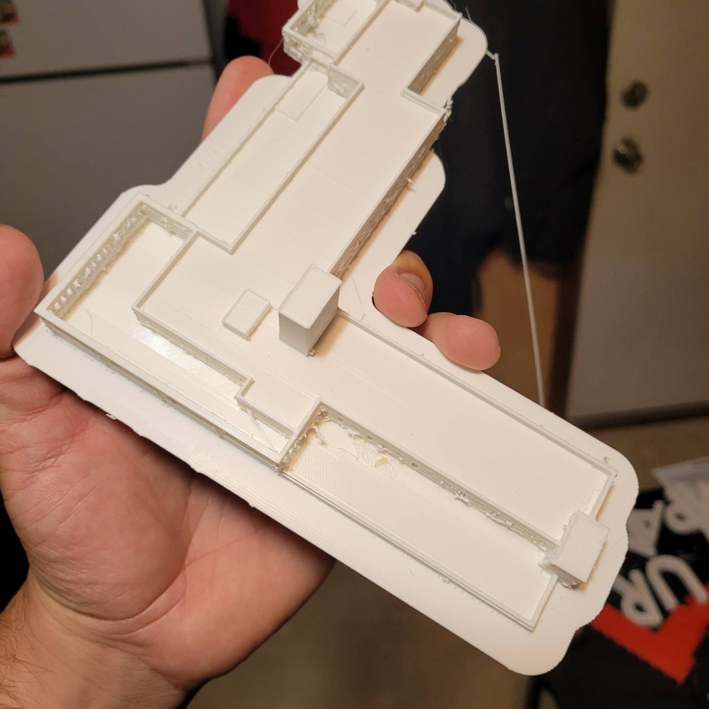 A hand holding a white 3D printed building section fresh off the printer