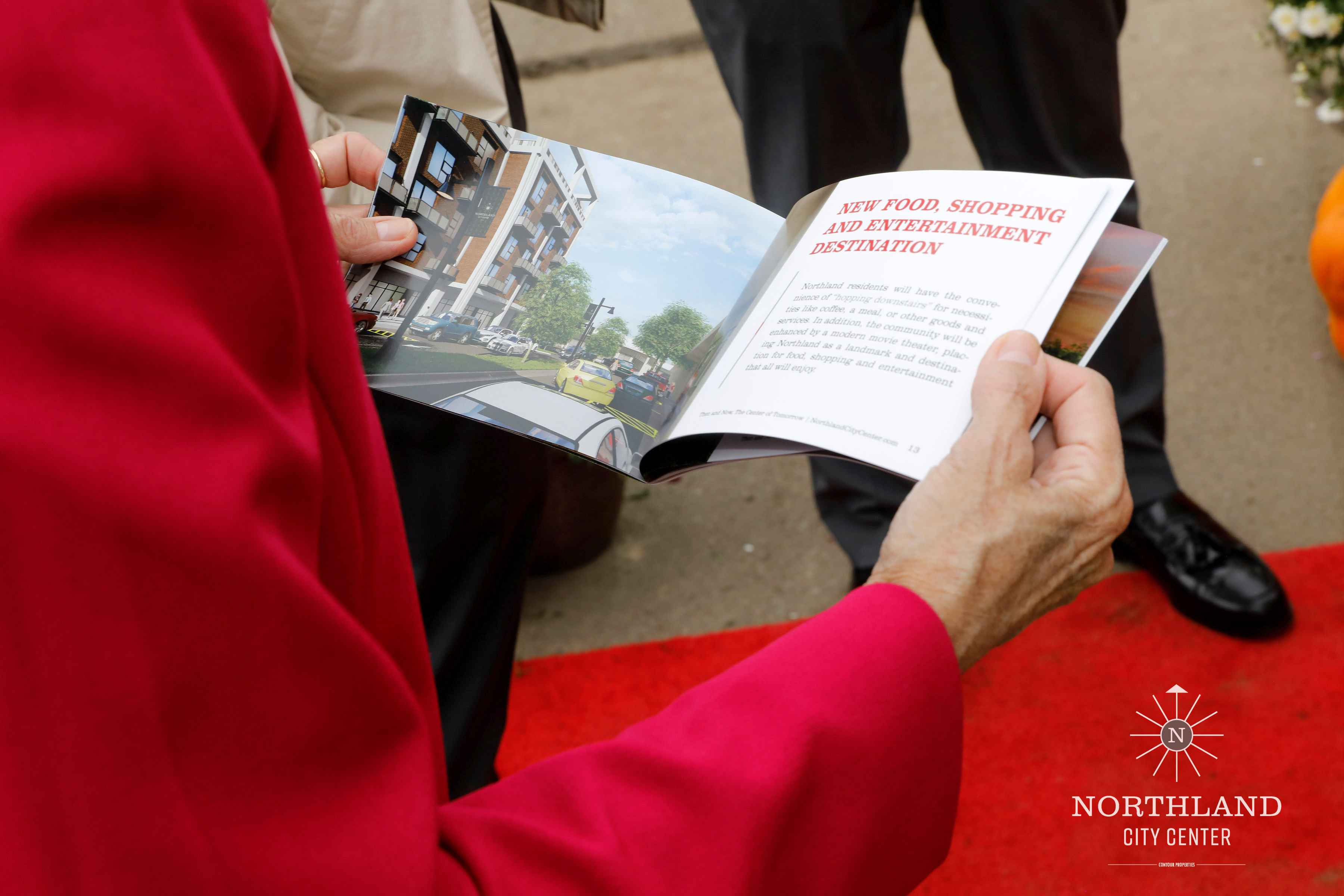 A guest holding open the printed Northland City Center booklet showing renderings of the development