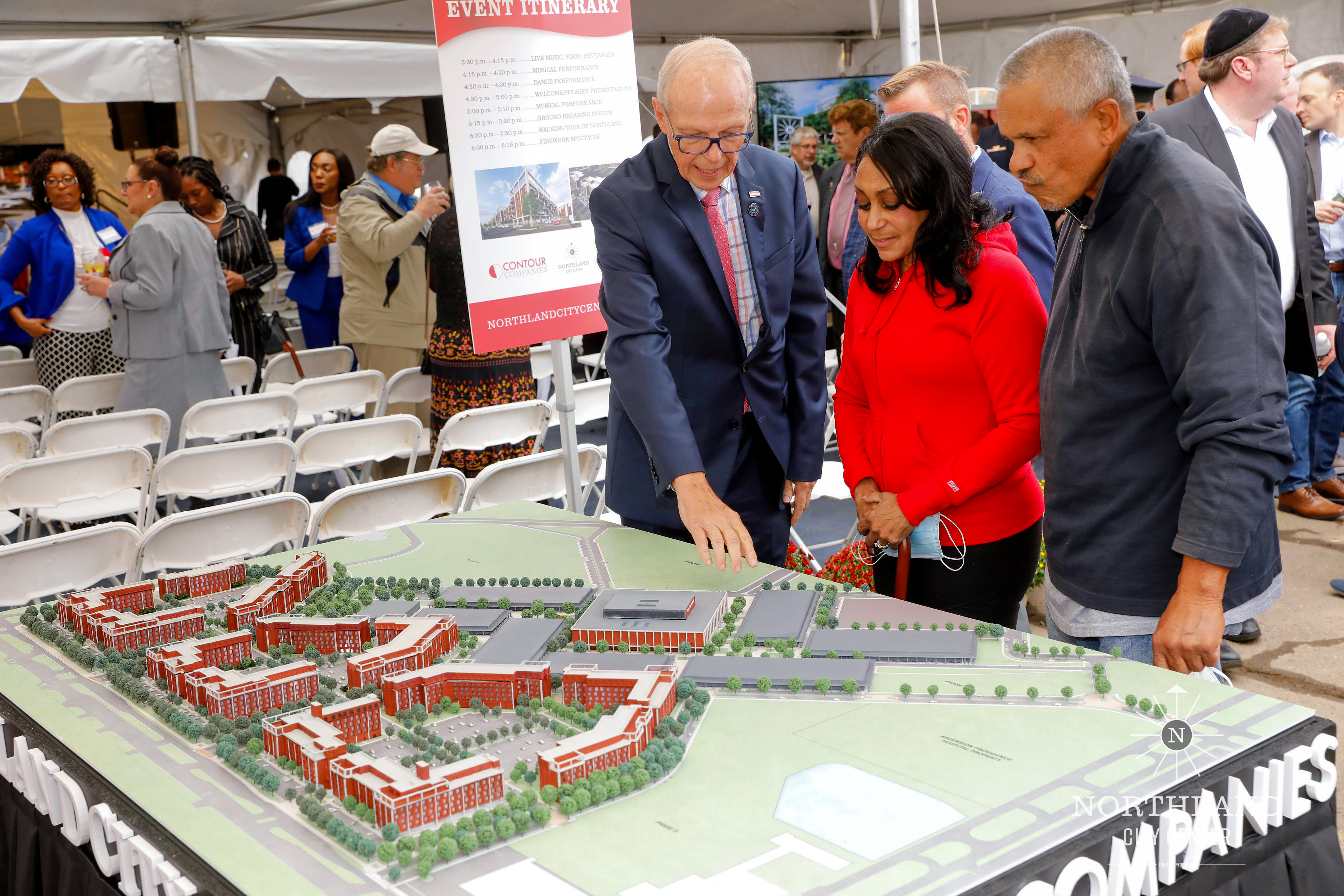 Guests in coats leaning over the Northland City Center model at the groundbreaking ceremony