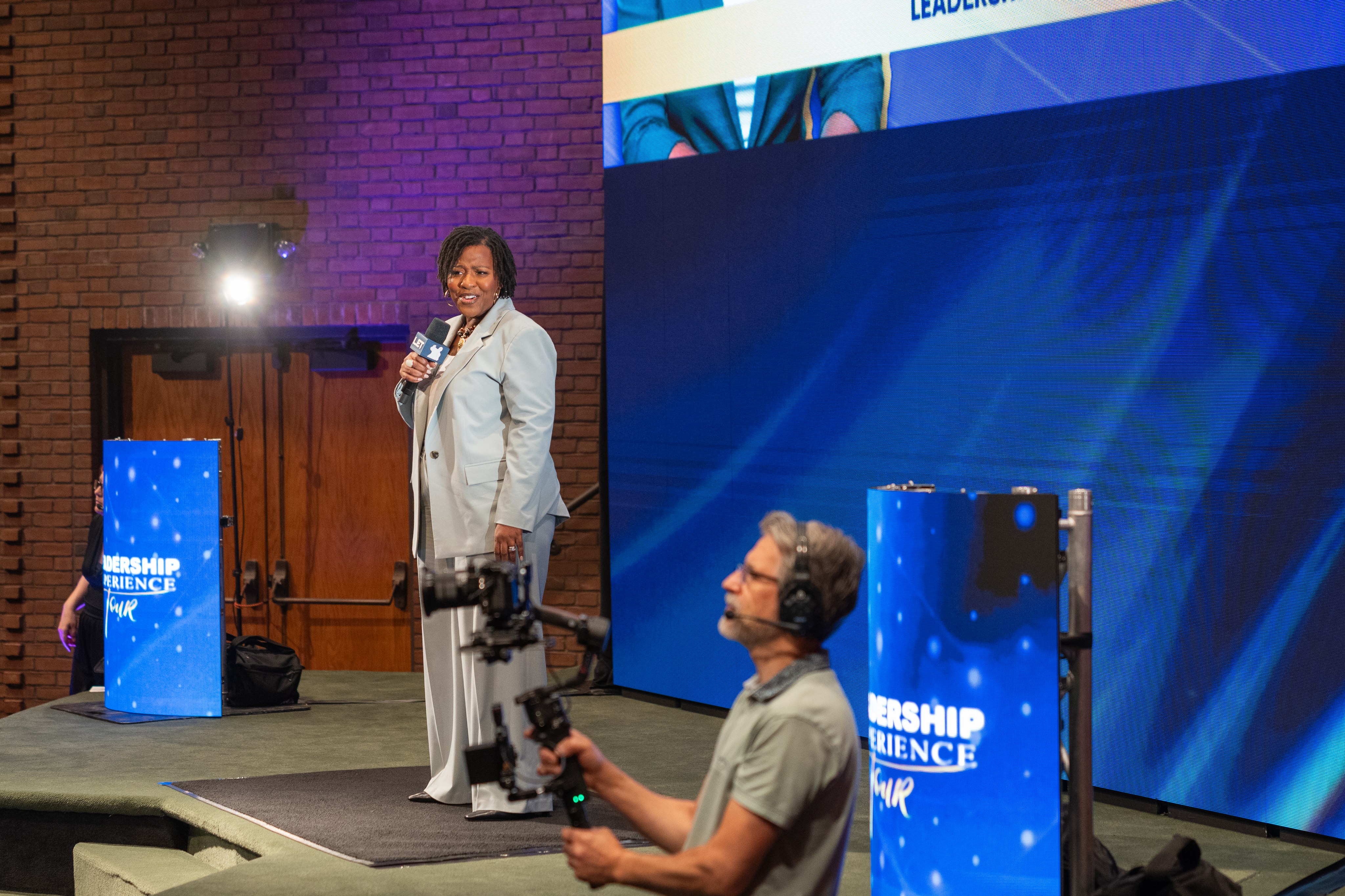 A speaker on stage while an operator films from a gimbal in the foreground