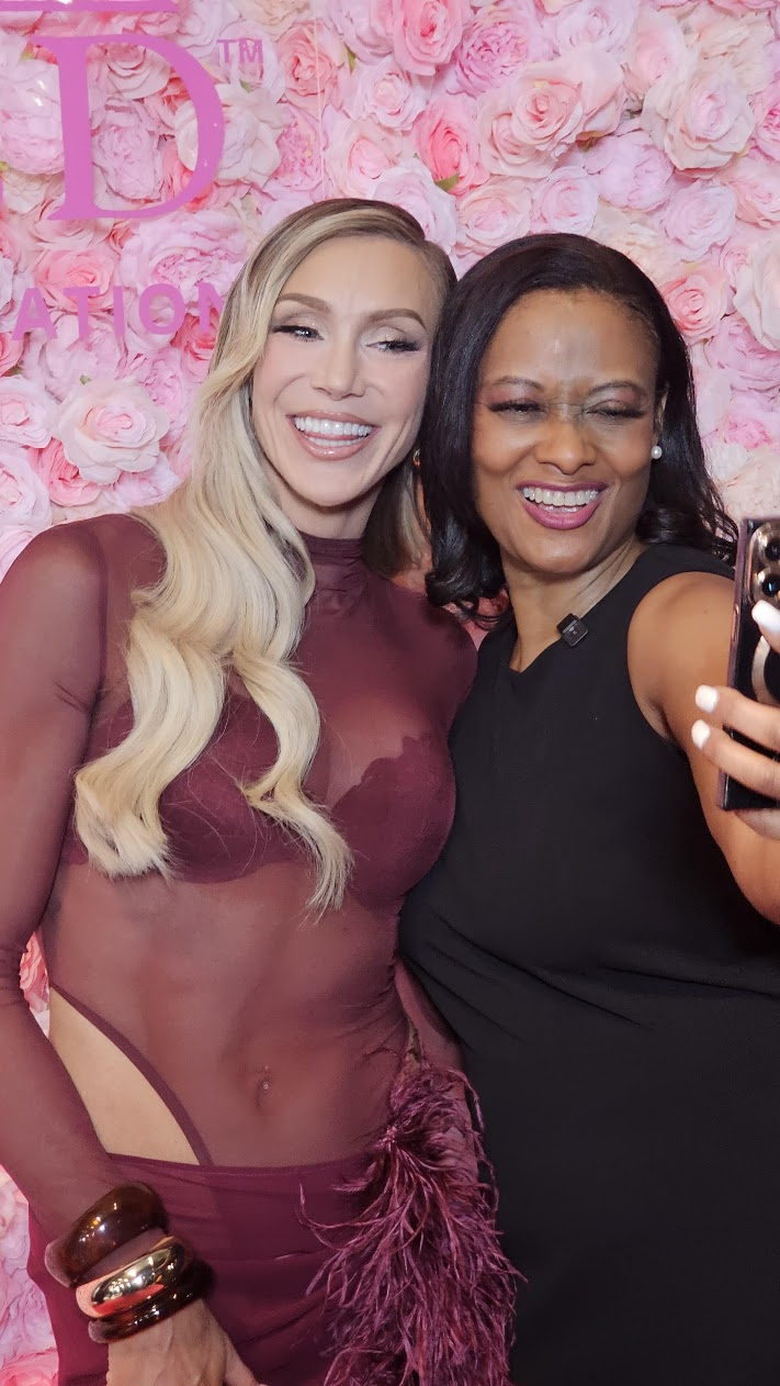 Charlotte Flair and Dr. Marcea Whitaker smiling together for a selfie in front of a wall of pink roses