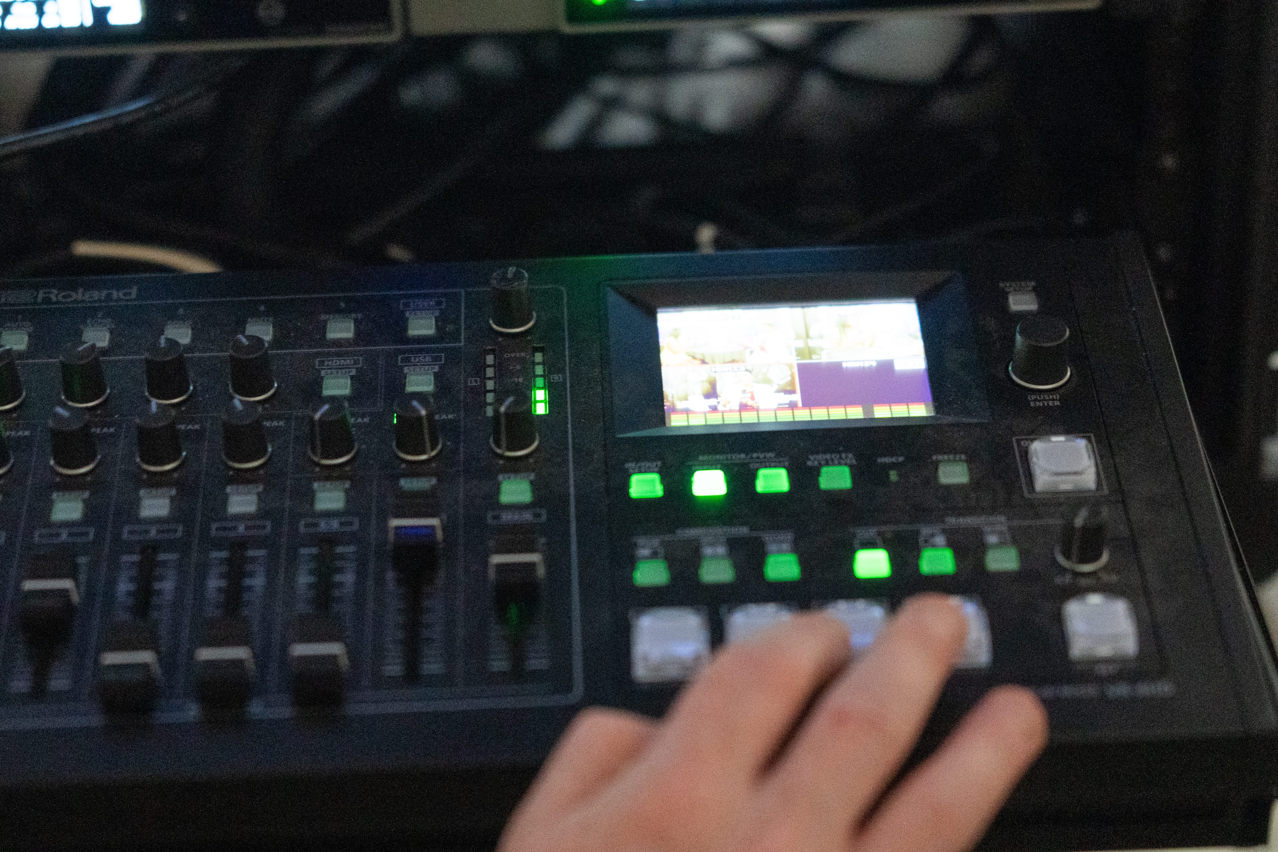 A hand on the faders of a Roland VR-4HD switcher during a live broadcast