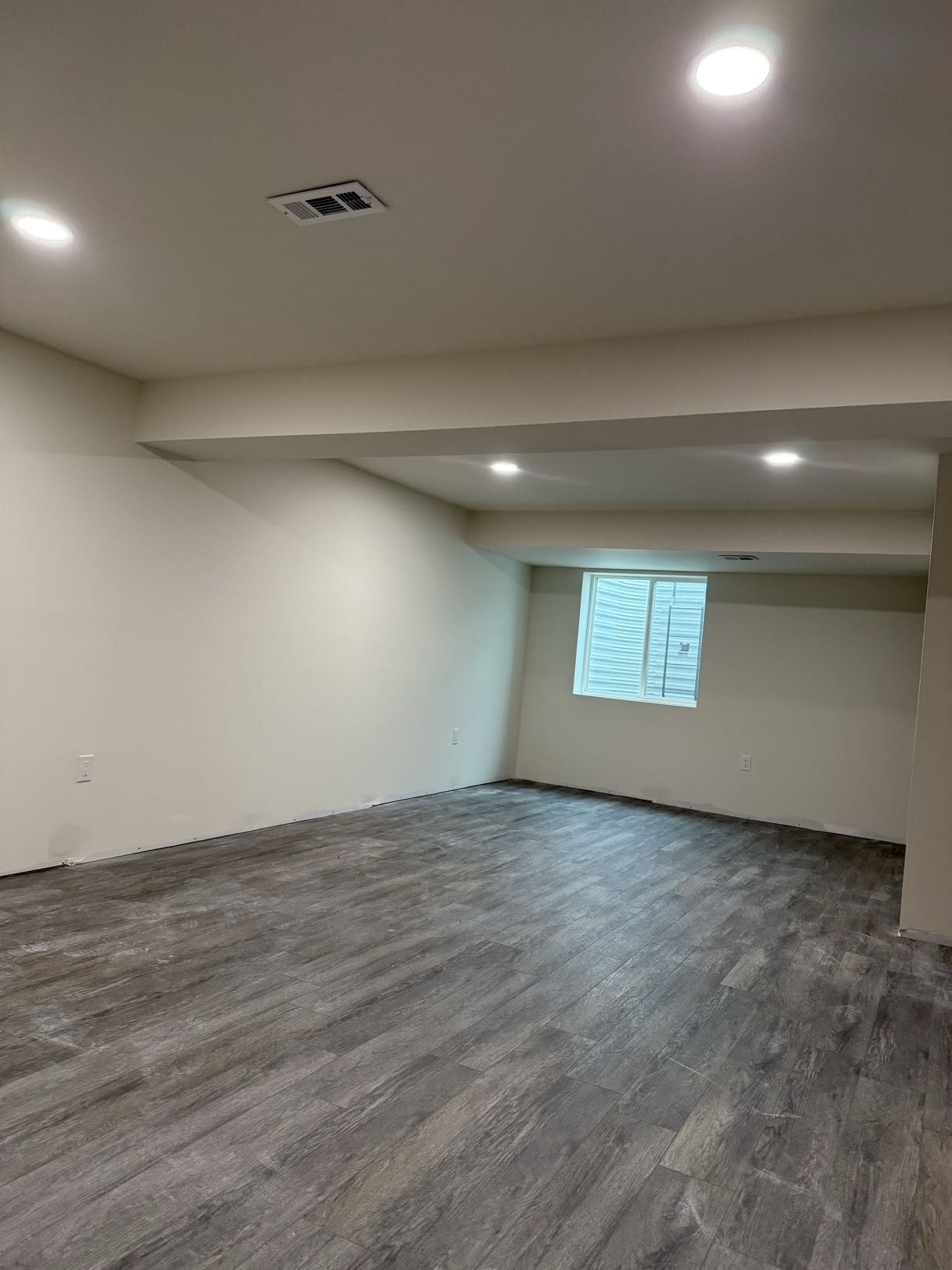Finished basement remodel with painted walls, recessed lights, soffit details, and gray plank flooring.