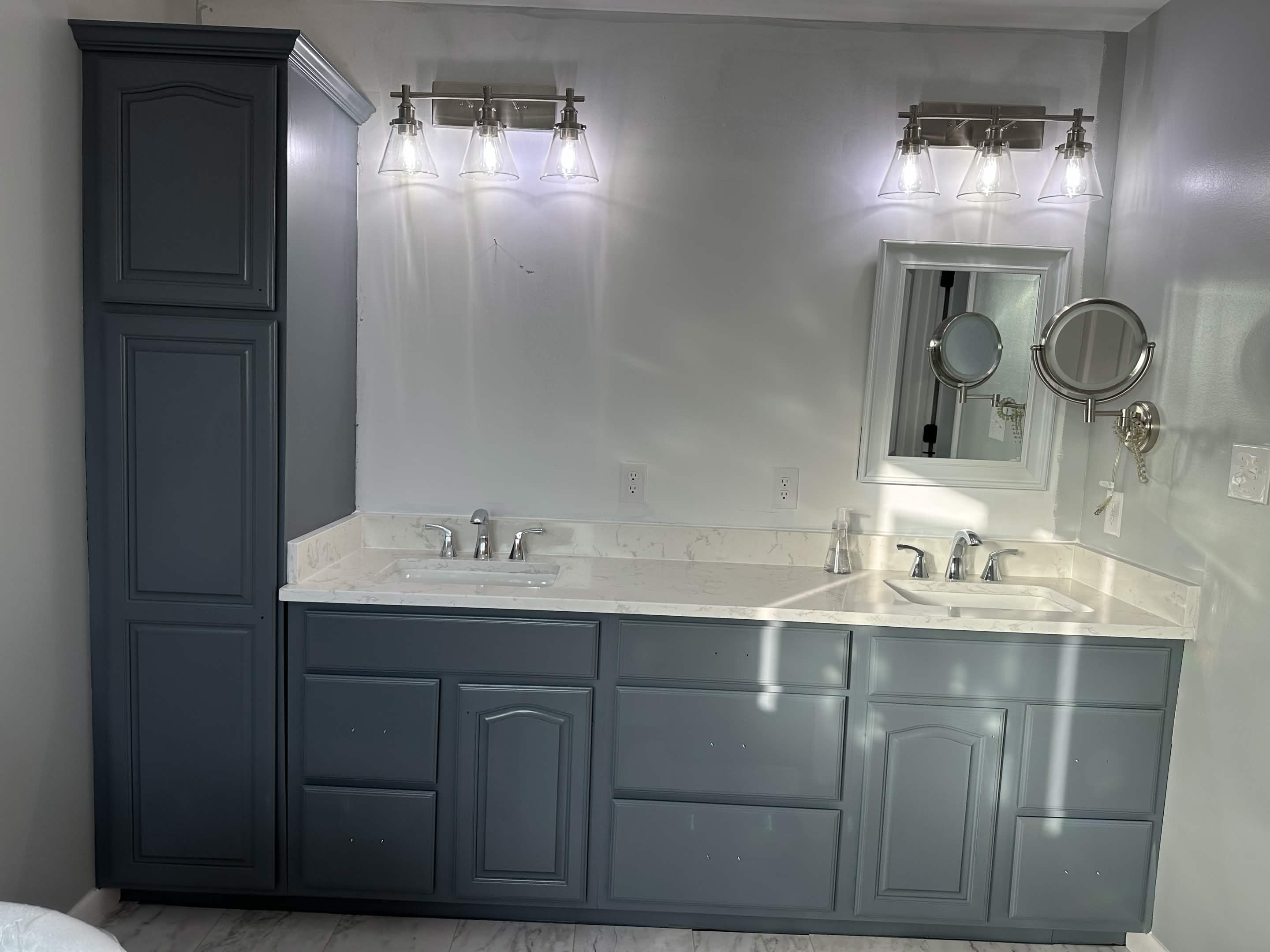 Bathroom remodel with painted dual-sink vanity cabinetry, tower storage, and upgraded lighting.