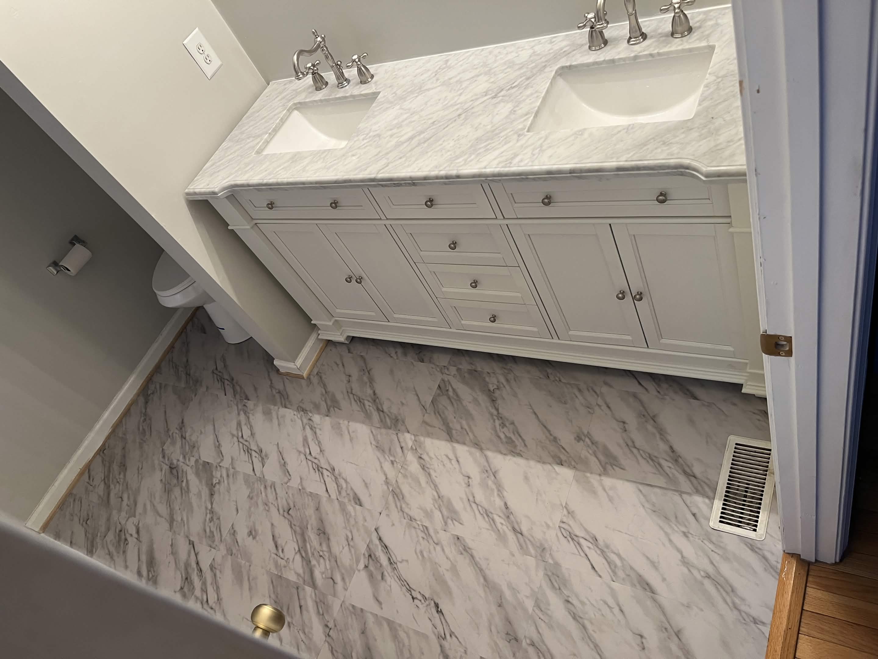 Bathroom remodel with a white double-sink vanity, marble-look countertop, and large-format floor tile.