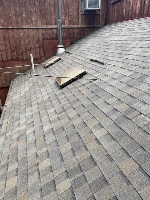 Completed asphalt shingle roof section with flashing details around vents and wall transitions.