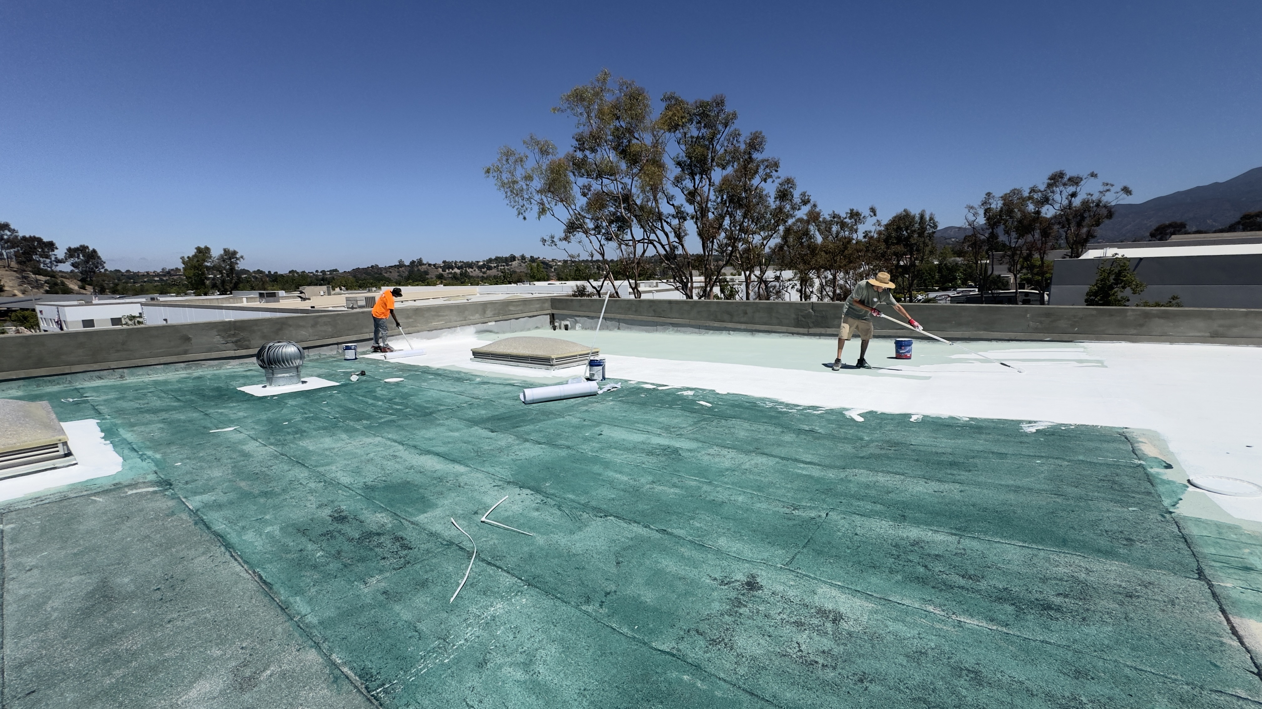 Worker coating a roof beside a tree