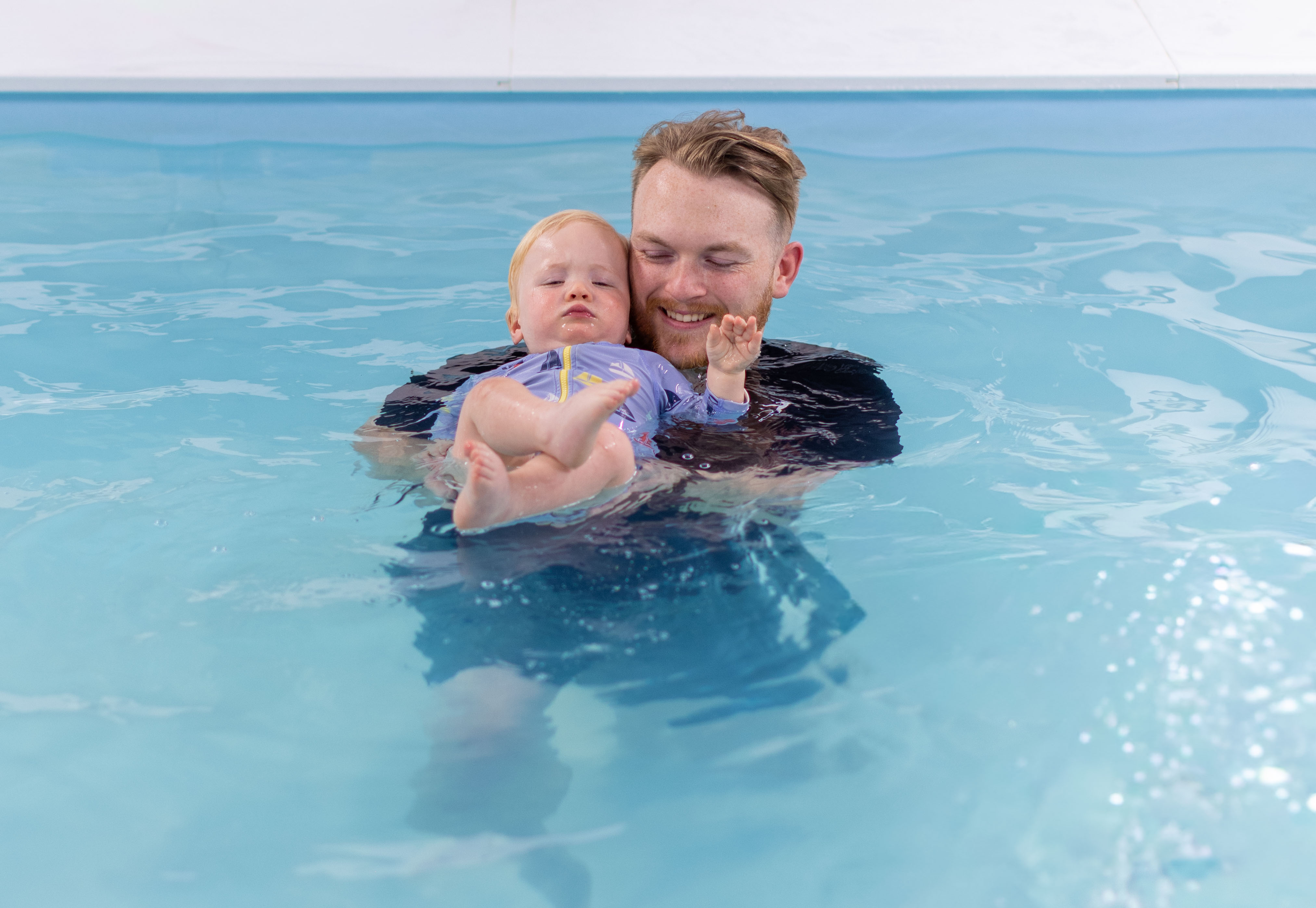 Instructor watching proudly as a toddler reaches for the pool wall
