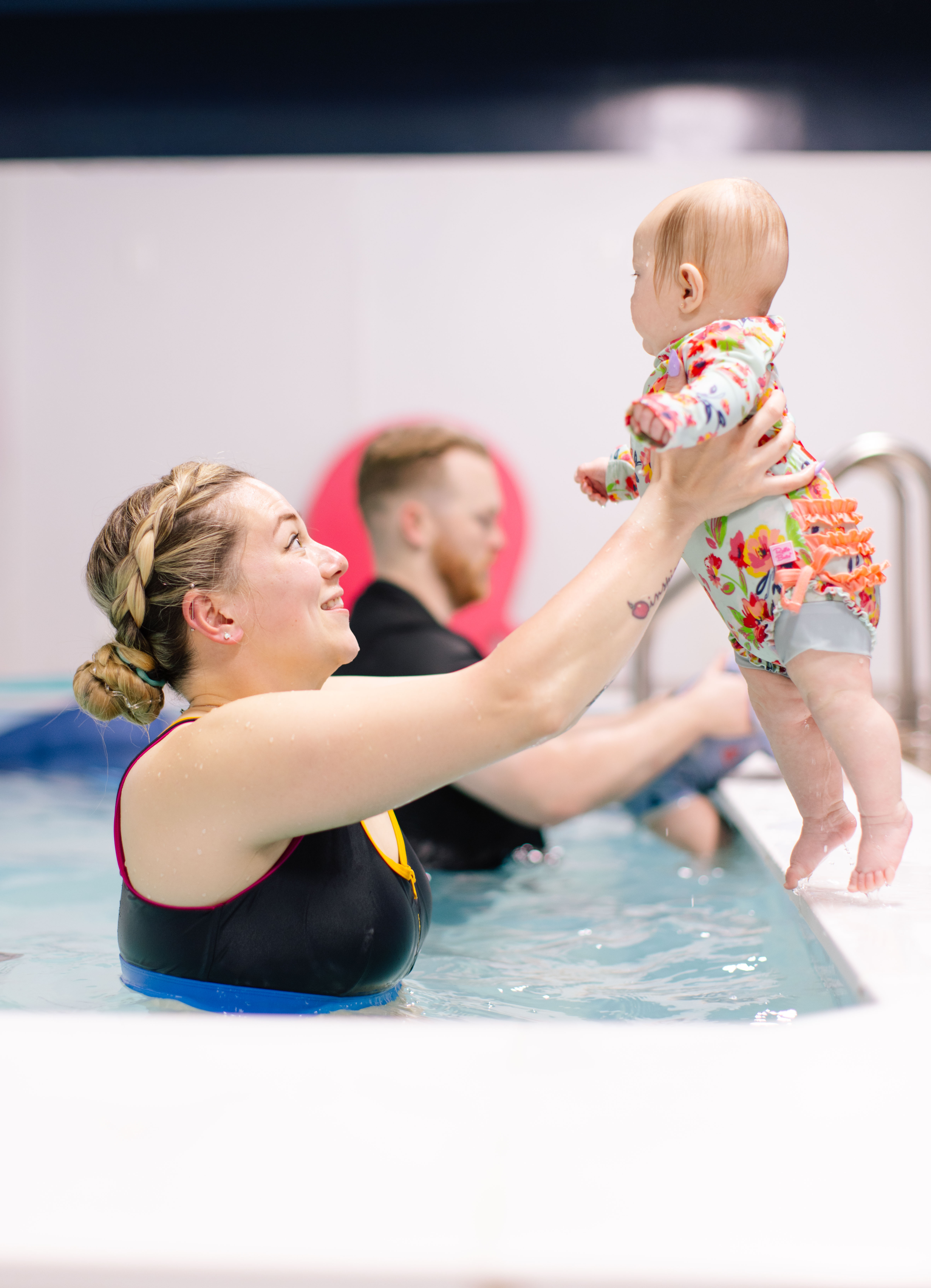 Instructor hoisting a baby in a floral swim onesie high above the water