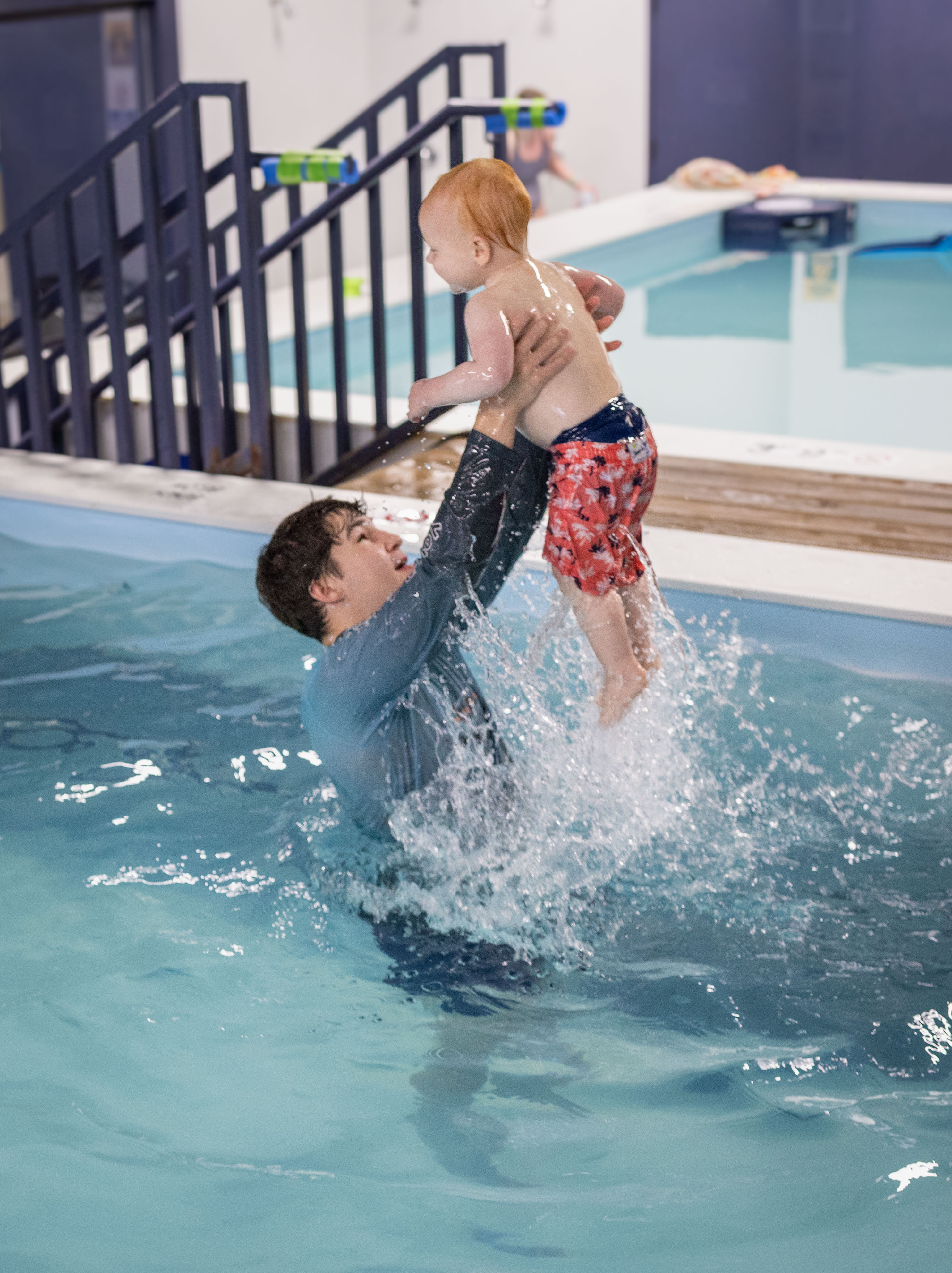 Teen coach hoists a toddler high above the pool as splashes erupt