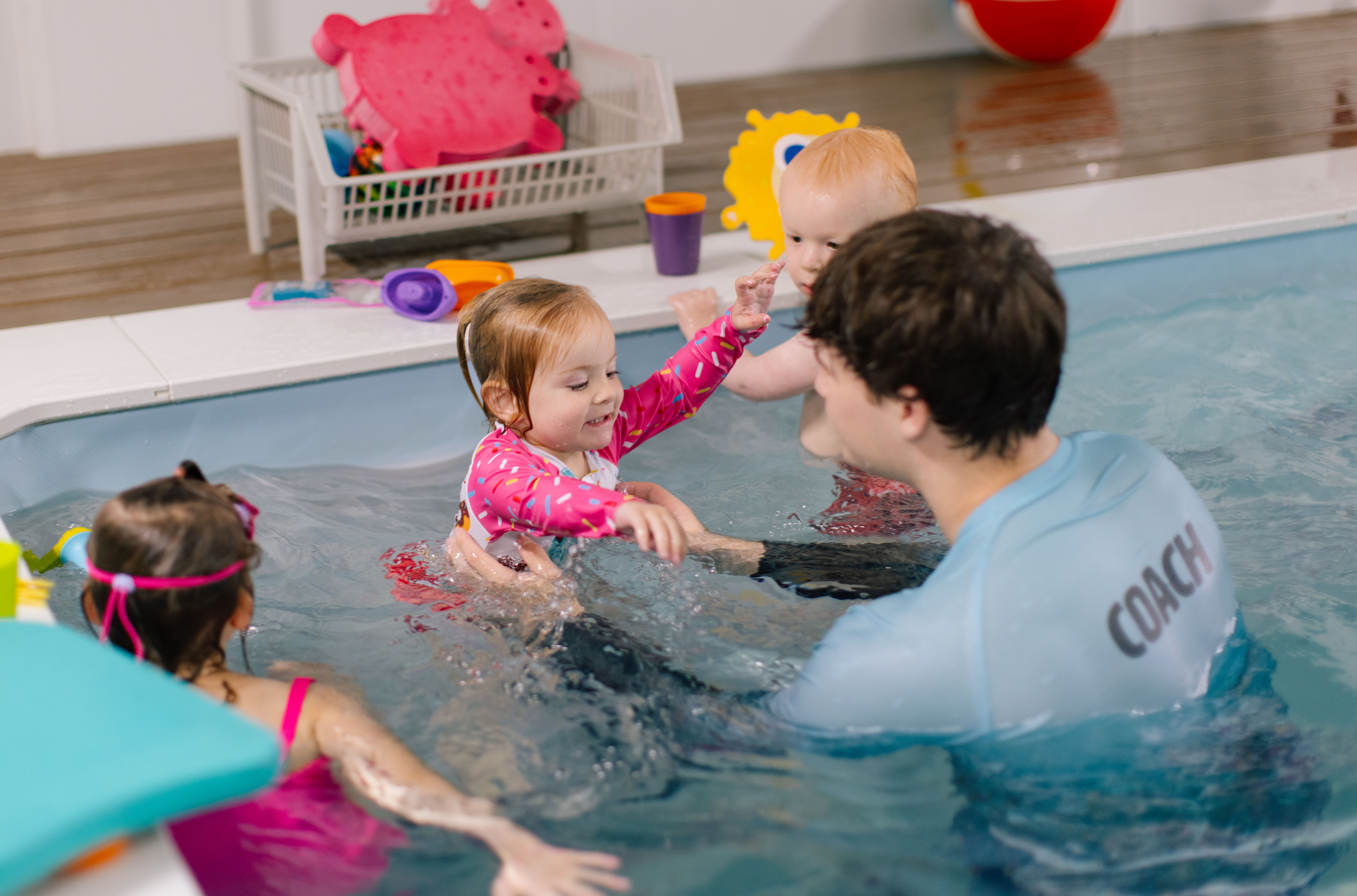 Coach playing with two toddlers while a sibling looks on through pink goggles