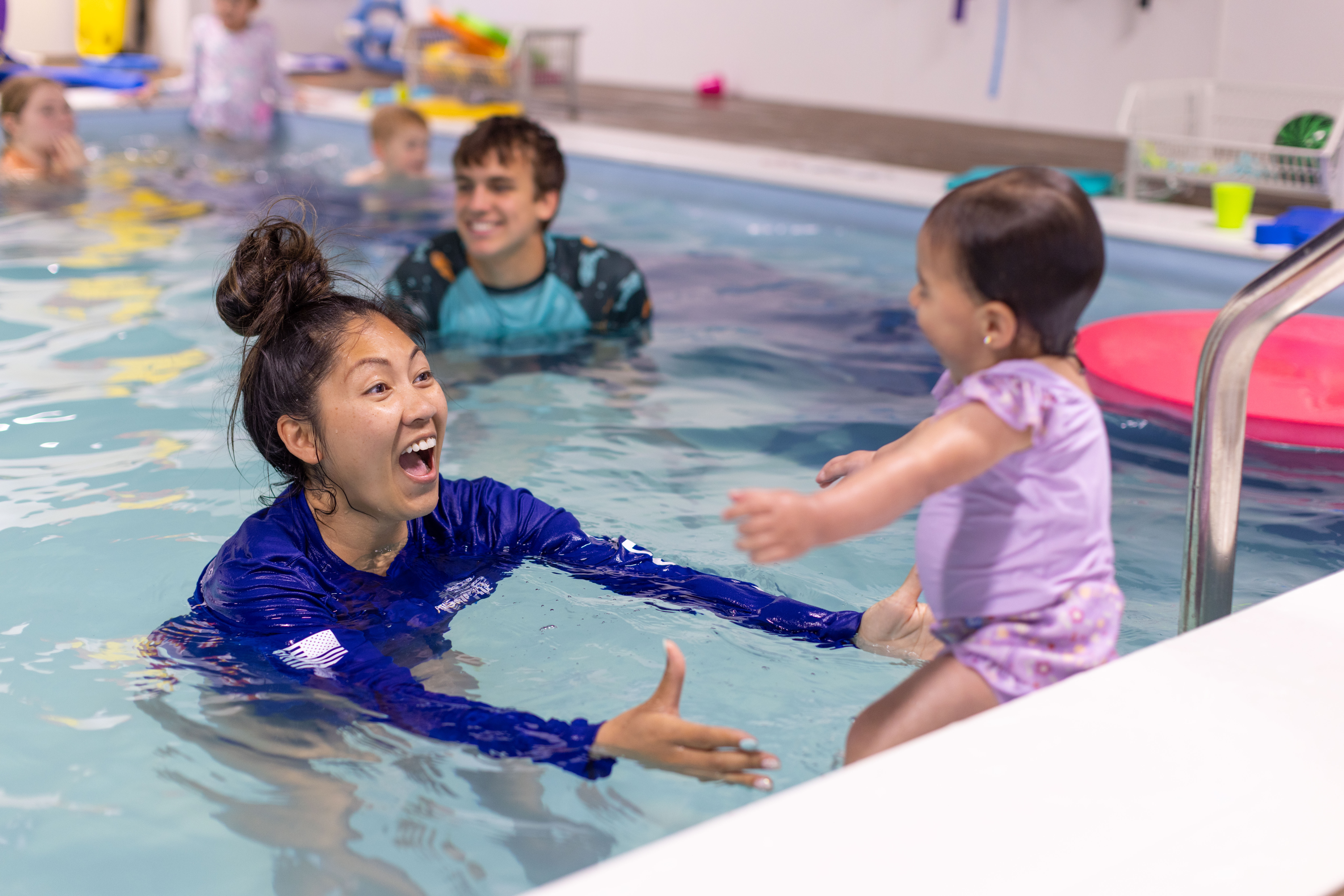 Instructor laughing as she reaches toward a toddler in the pool