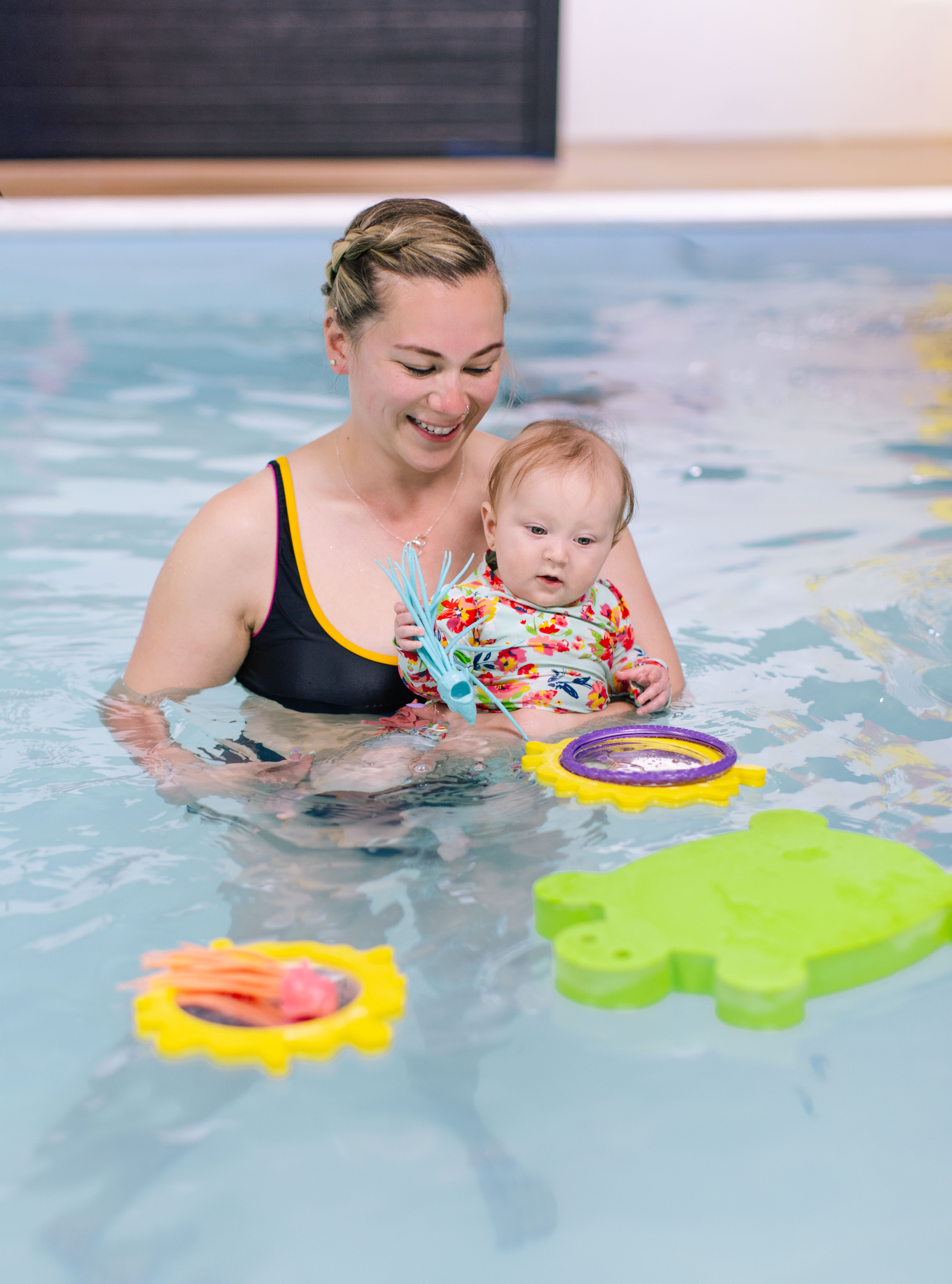 Instructor holds a baby chest-to-chest as they watch a dive ring float by