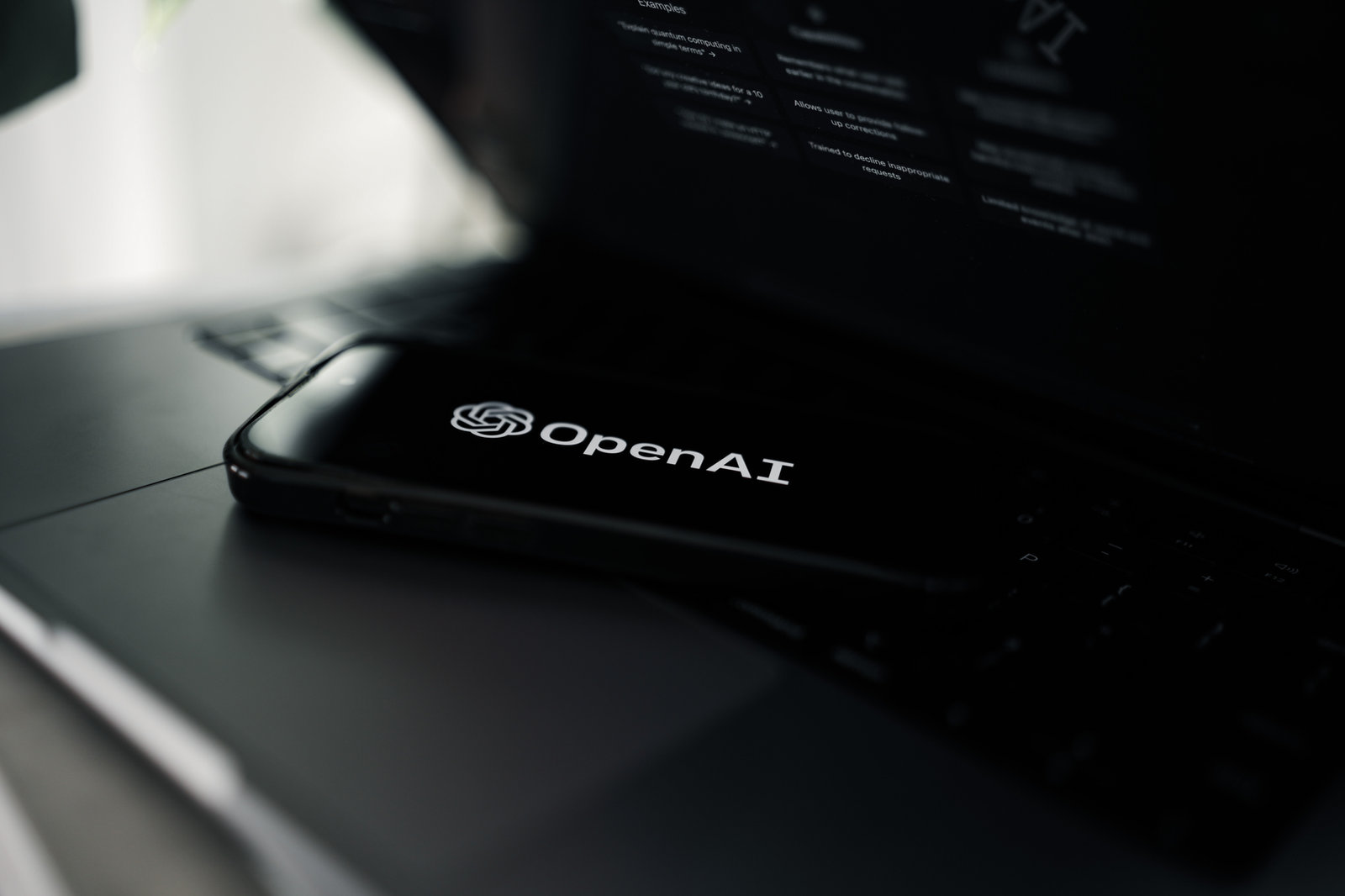 OpenAI logo on a phone sitting on a laptop