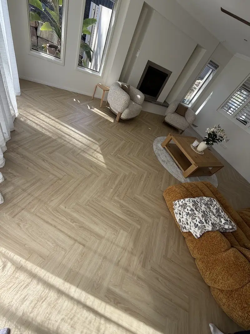 Herringbone flooring installed through a living room with fireplace and tall windows