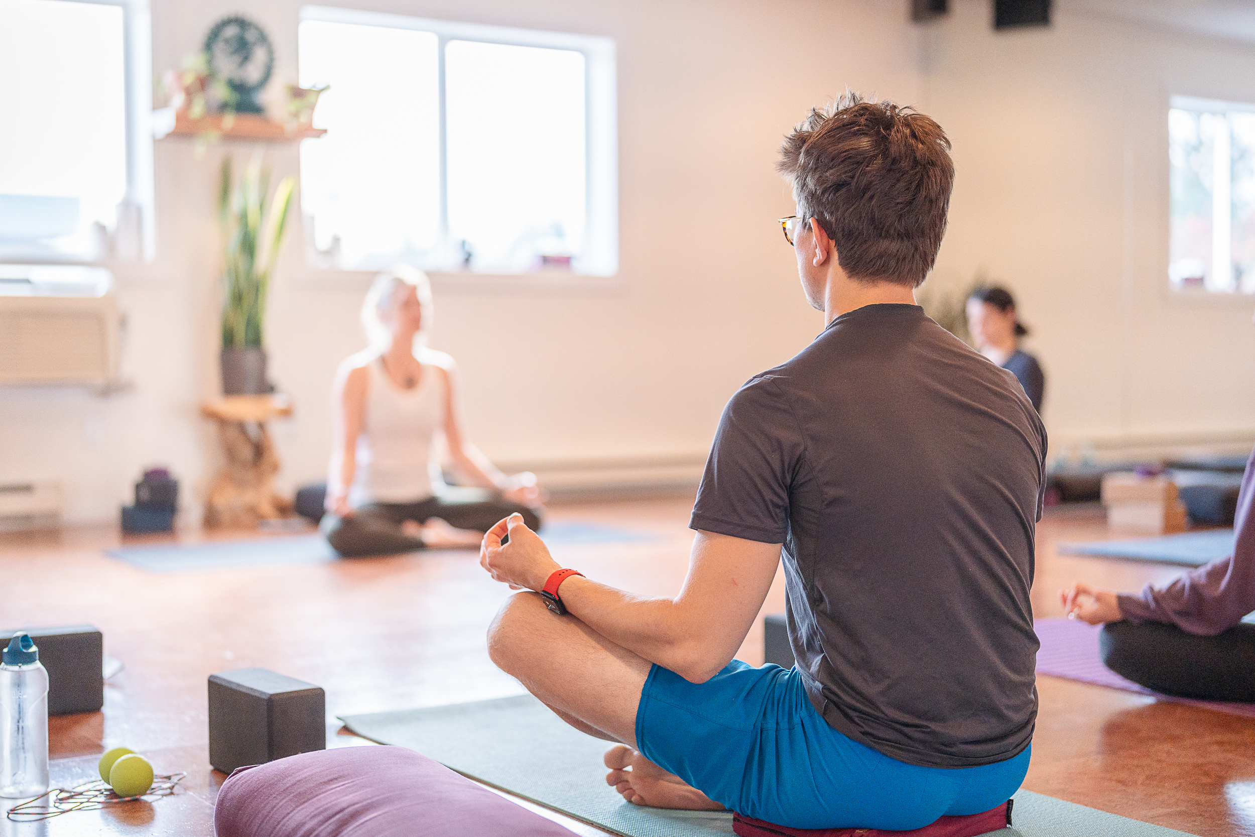 Focused yoga participants engaged in a meditation session, with a man in the foreground in a cross-legged pose, embodying mindfulness and serenity at a Squamish yoga studio.