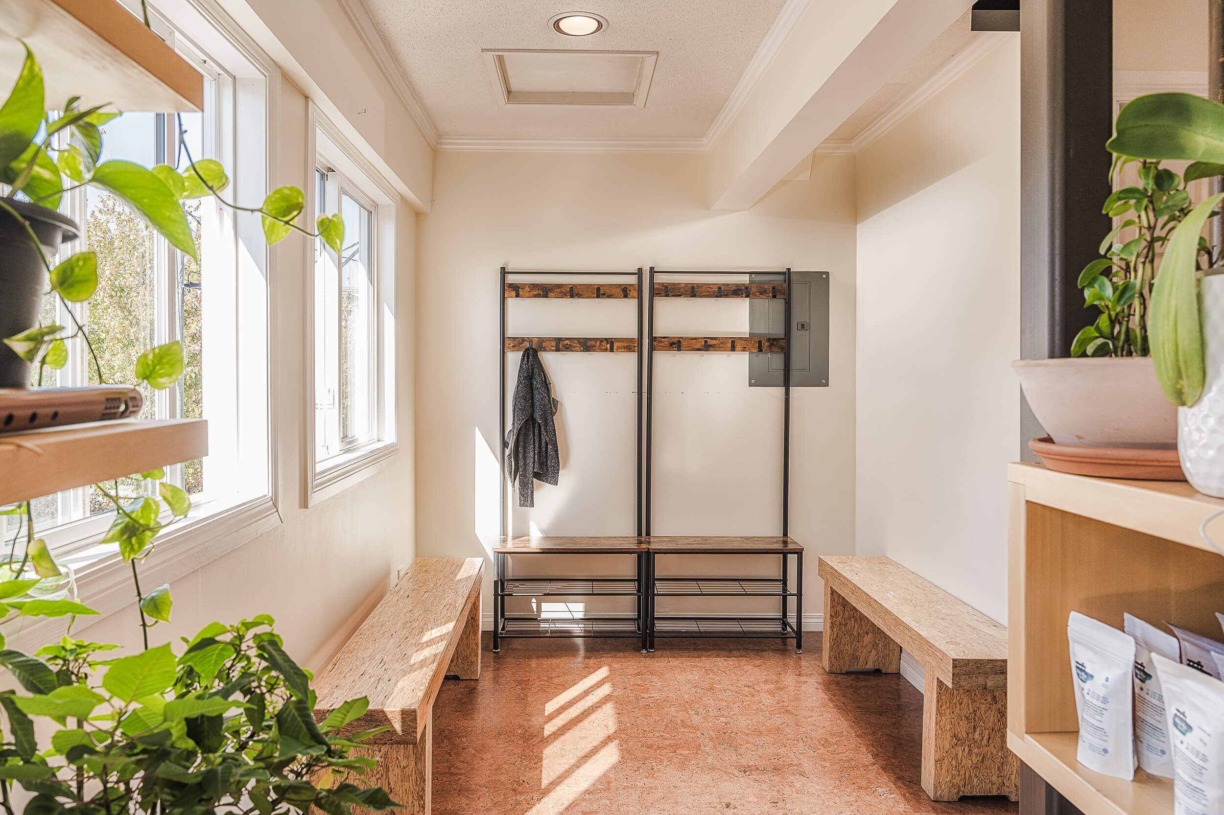 Sunlit entrance of Shala Yoga studio in Squamish featuring natural wood benches, a plant-filled shelf, and a rack with yoga accessories. The welcoming atmosphere is enhanced by the warm glow through large windows, creating a serene space for yogis to gather before class.