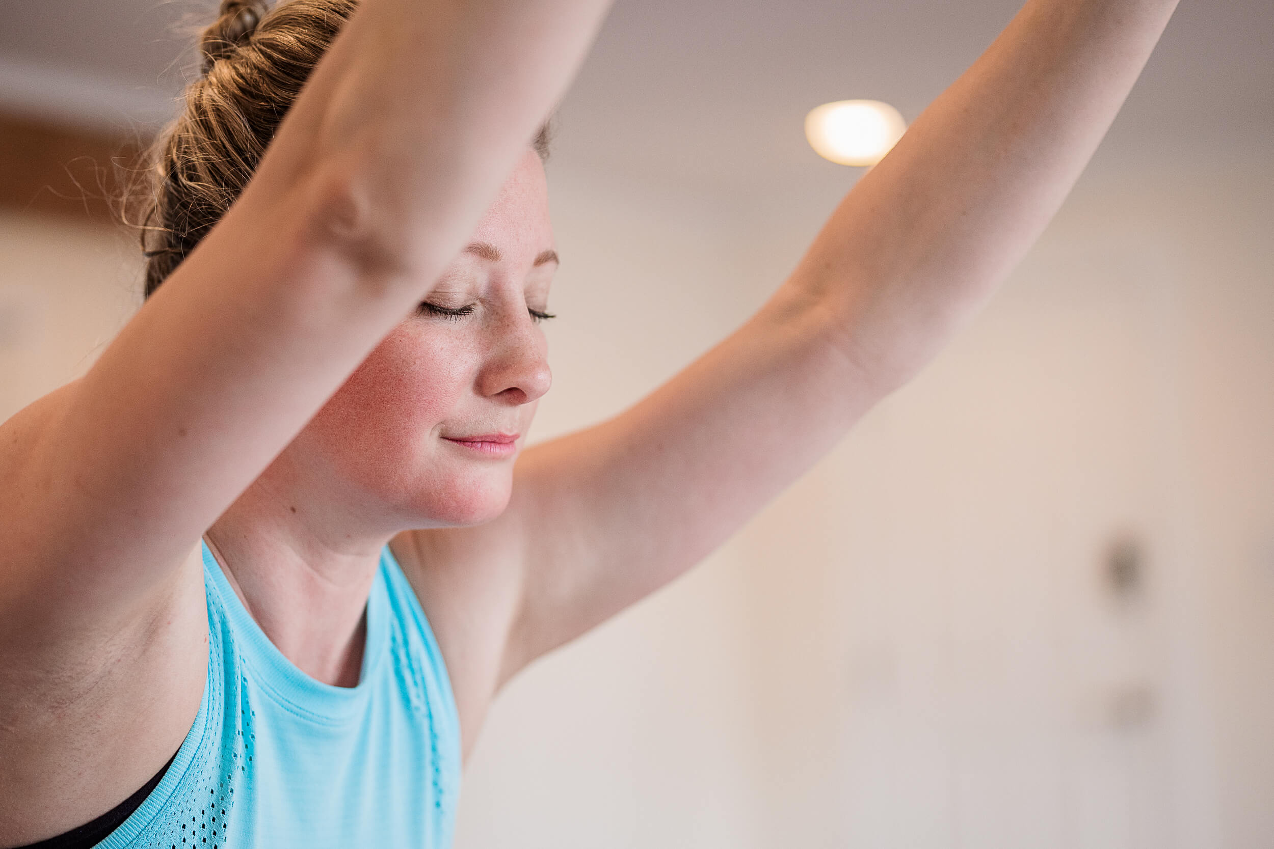 A close-up of a serene yoga student with closed eyes, arms raised gracefully overhead, embodying a sense of calm and focus during a yoga session at Shala Yoga studio in Squamish