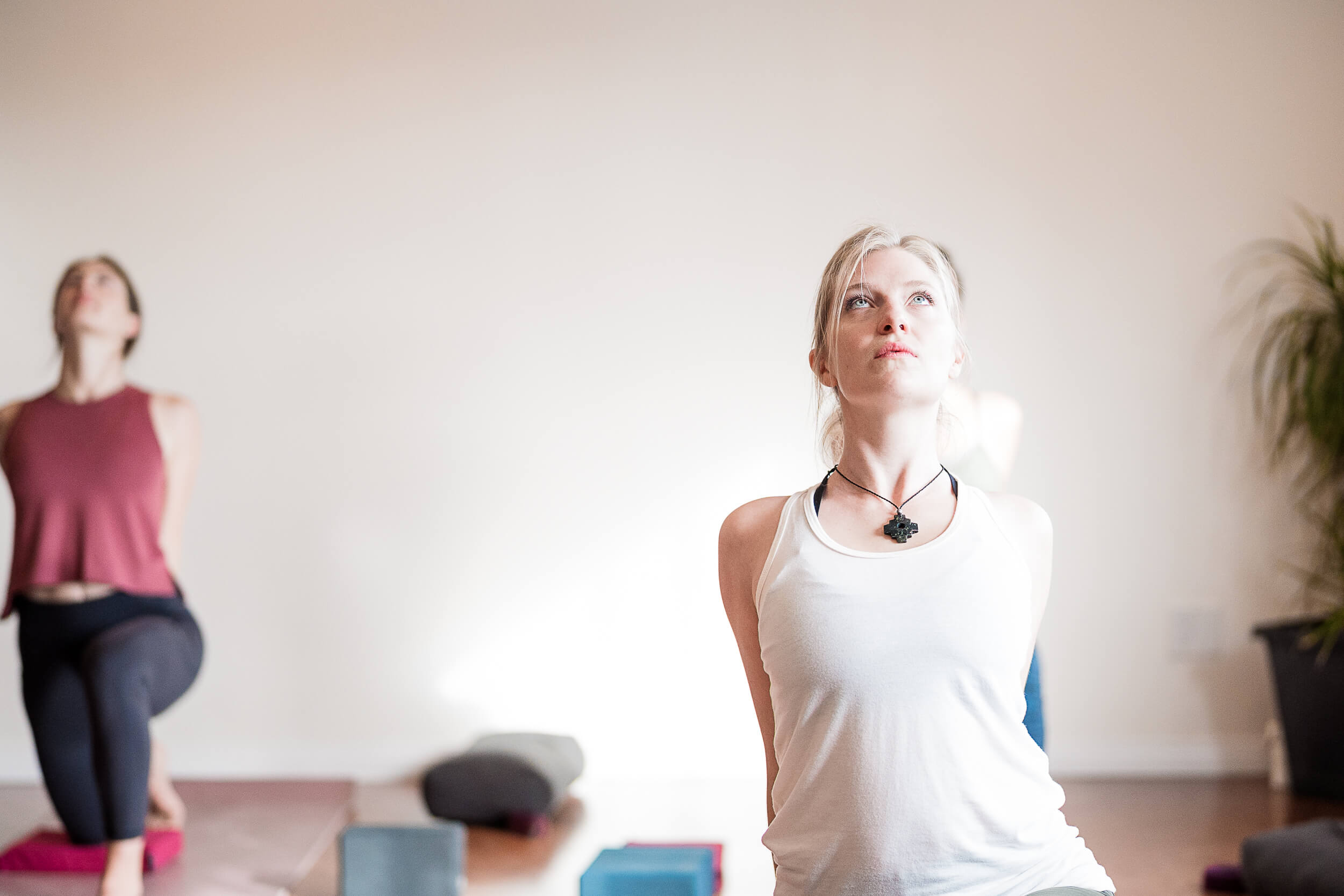 A person in a white tank top performs a yoga pose with a gaze upward, embodying tranquility and focus at Shala Yoga studio in Squamish, with soft natural light enhancing the calm atmosphere.
