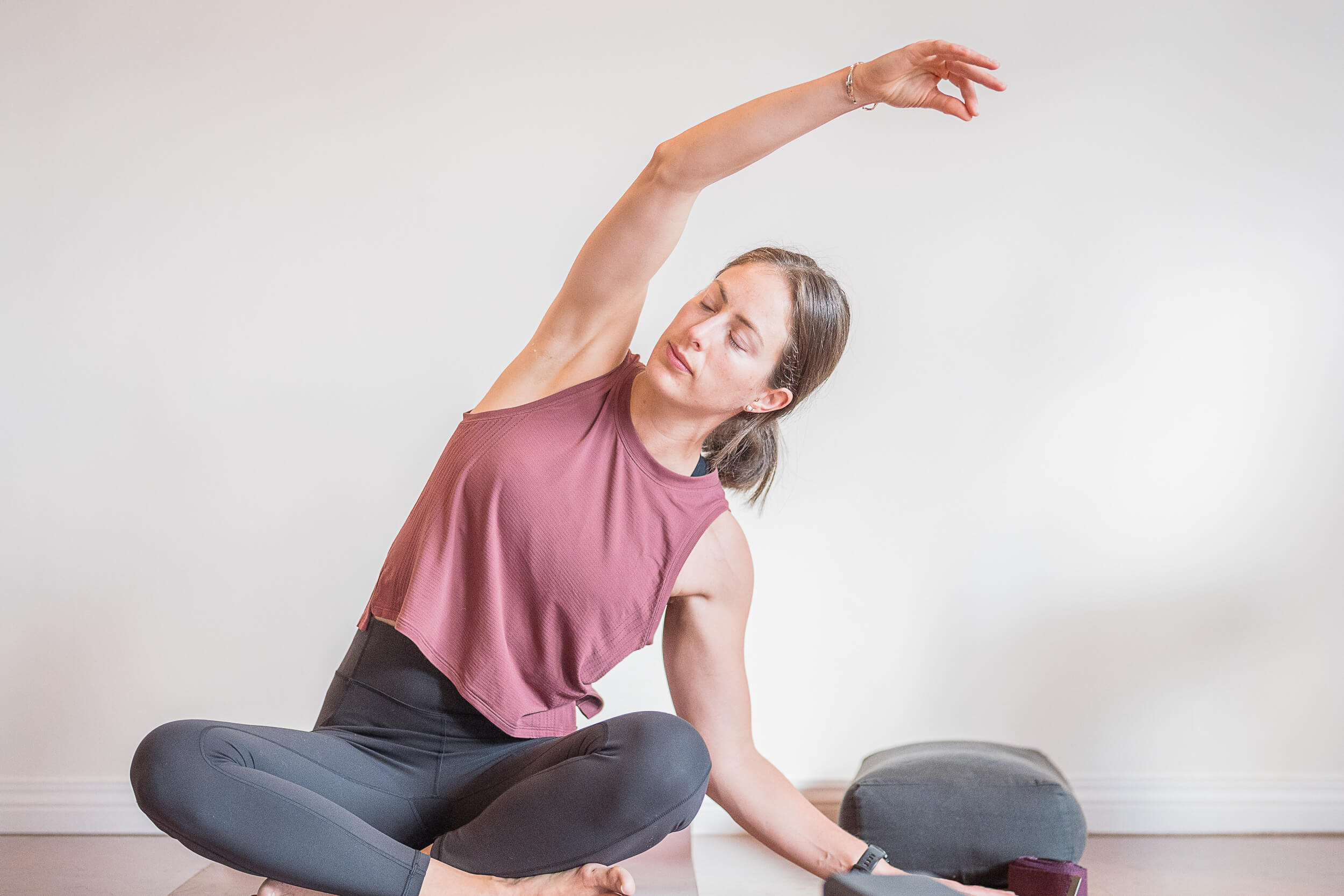 Yoga instructor demonstrates a seated side stretch, with extended arm creating a graceful line, focused and serene in a peaceful yoga studio setting, indicative of the classes at Shala Yoga studio in Squamish.