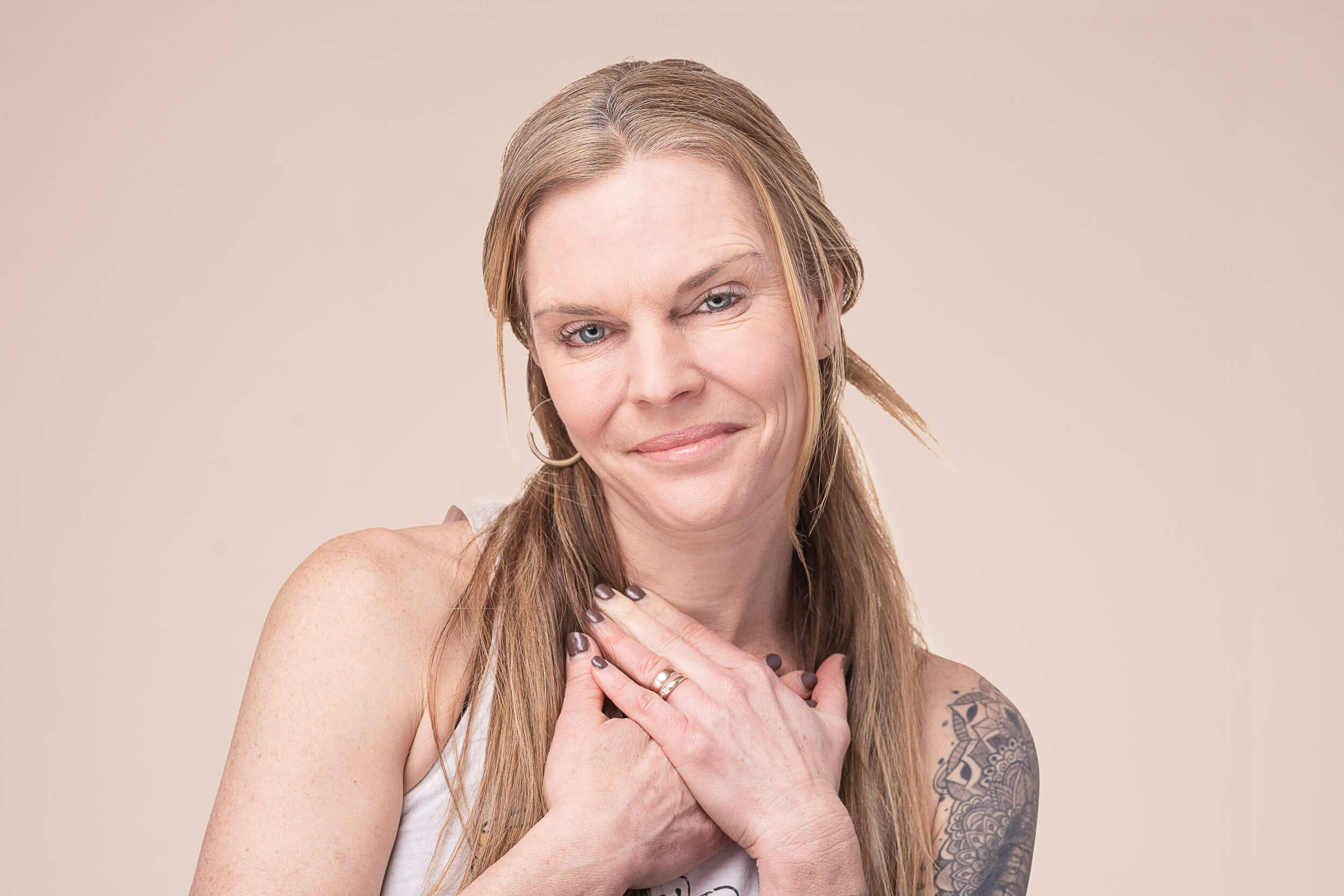 Experienced yoga instructor with a confident gaze and hands gently placed on heart, wearing a sleeveless top and showcasing her arm tattoo, representing the blend of strength and grace at Shala Yoga studio in Squamish.