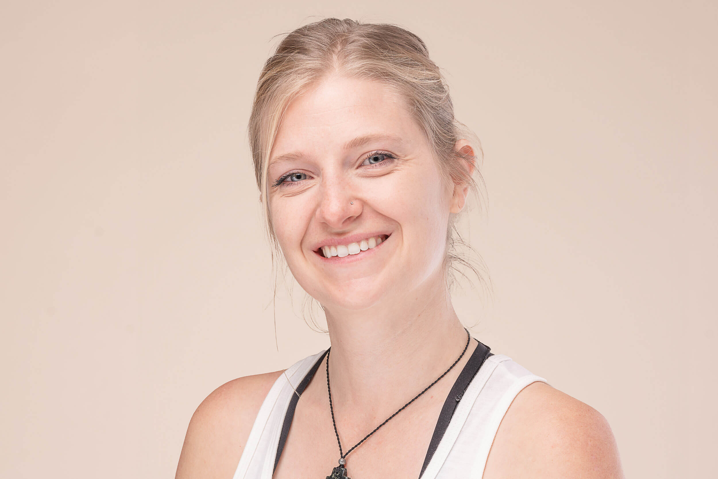 Smiling young yoga instructor in a white tank top with a relaxed and friendly demeanor, conveying the welcoming and inclusive spirit of Shala Yoga studio in Squamish.