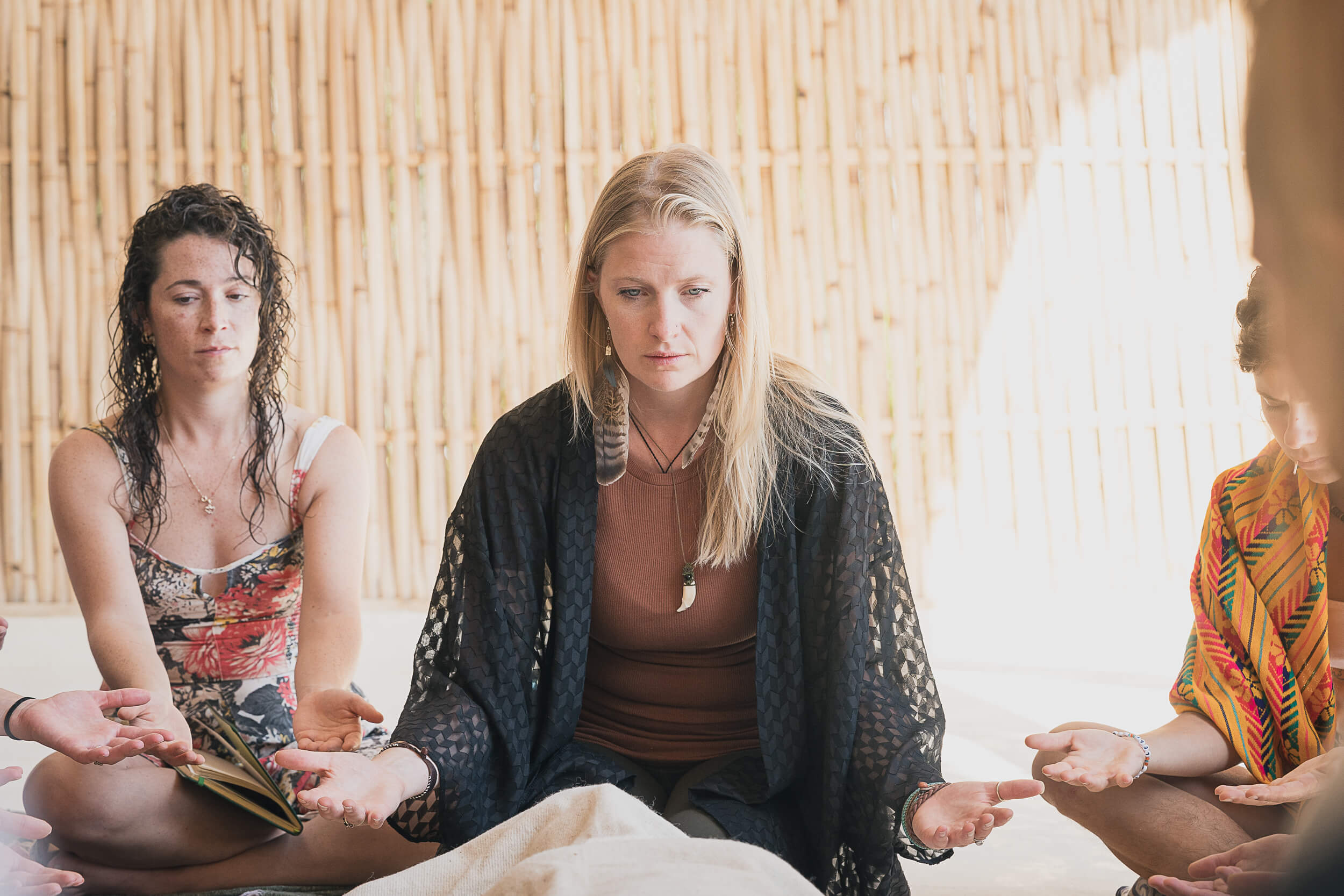 Three individuals engage in a serene meditation session, palms open in receiving mudra, in a space with bamboo background, reflecting the mindful ambiance of Shala Yoga studio in Squamish.