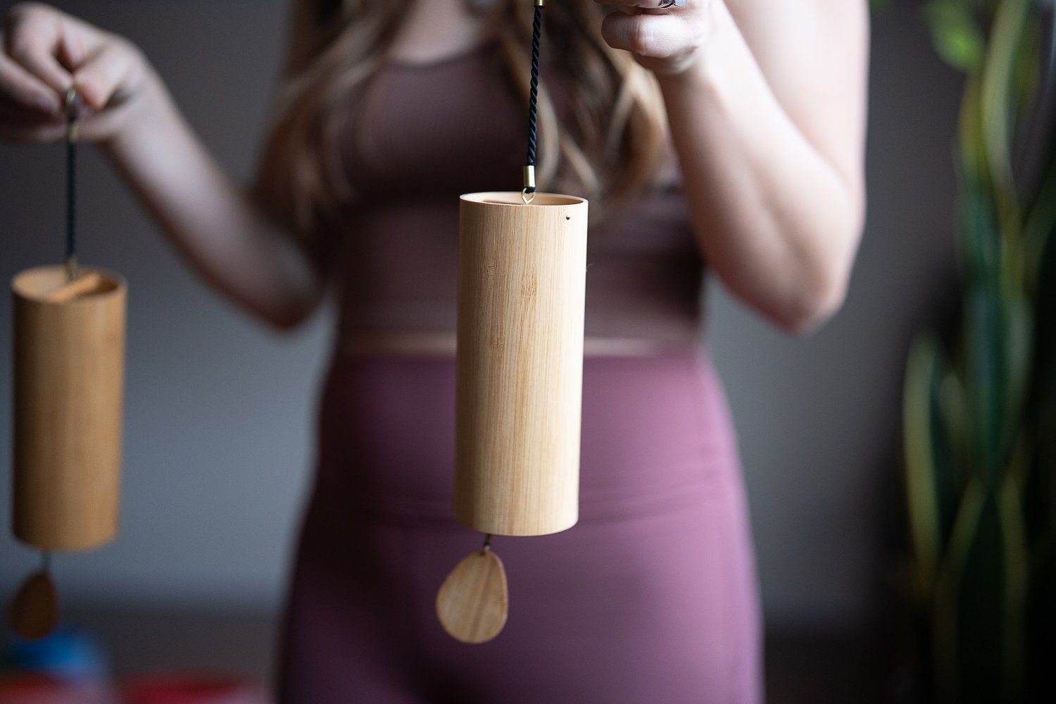 Close-up of a person holding two bamboo wind chimes, with a soft focus on the background, inside Shala Yoga studio, adding a peaceful, meditative ambience to the space in Squamish.