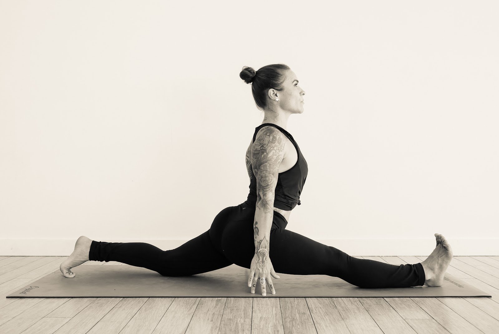 Monochrome image of a dedicated yoga instructor demonstrating an advanced split pose at Shala Yoga studio in Squamish, her tattoos adding to the artistic expression of strength and flexibility